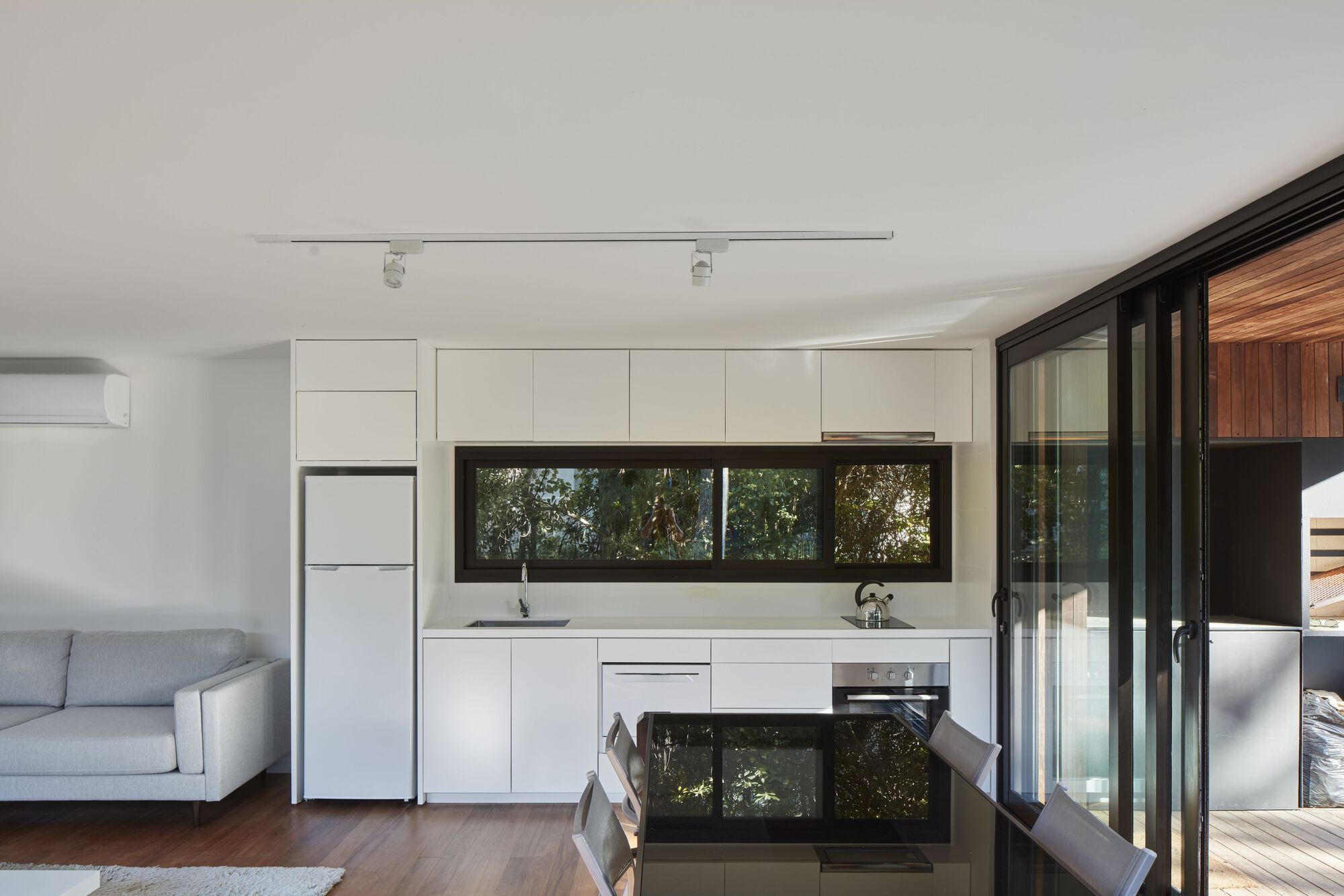 Open plan kitchen with white cabinetry, horizontal window and folding glass doors to timber deck