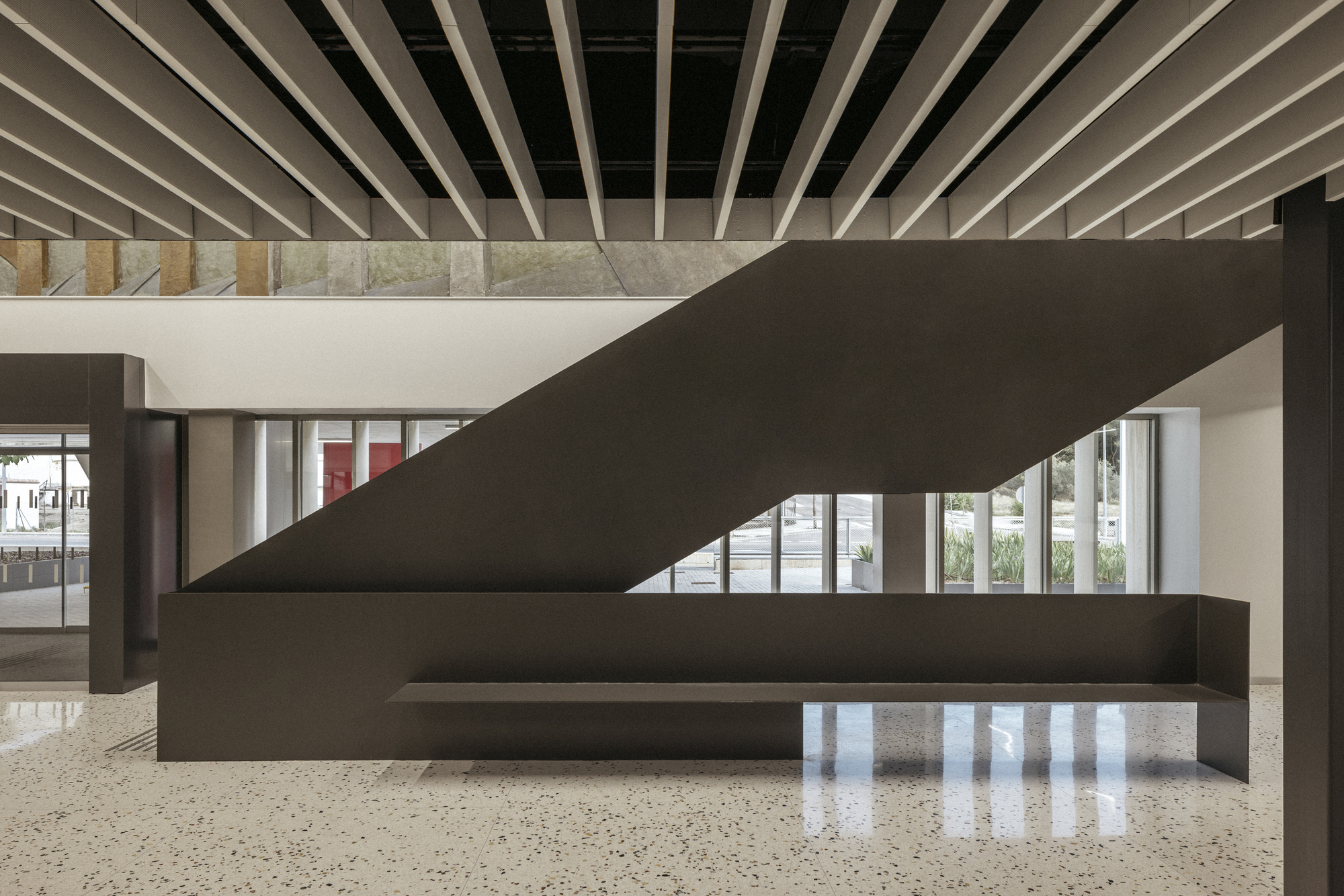 Interior lobby with dark steel staircase, terrazzo floor, and exposed timber ceiling joists