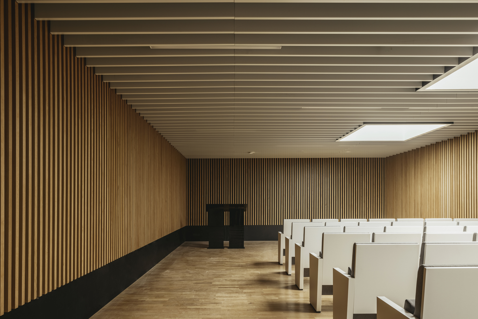 Interior assembly hall with vertical timber slat walls and ceiling and rows of white seating