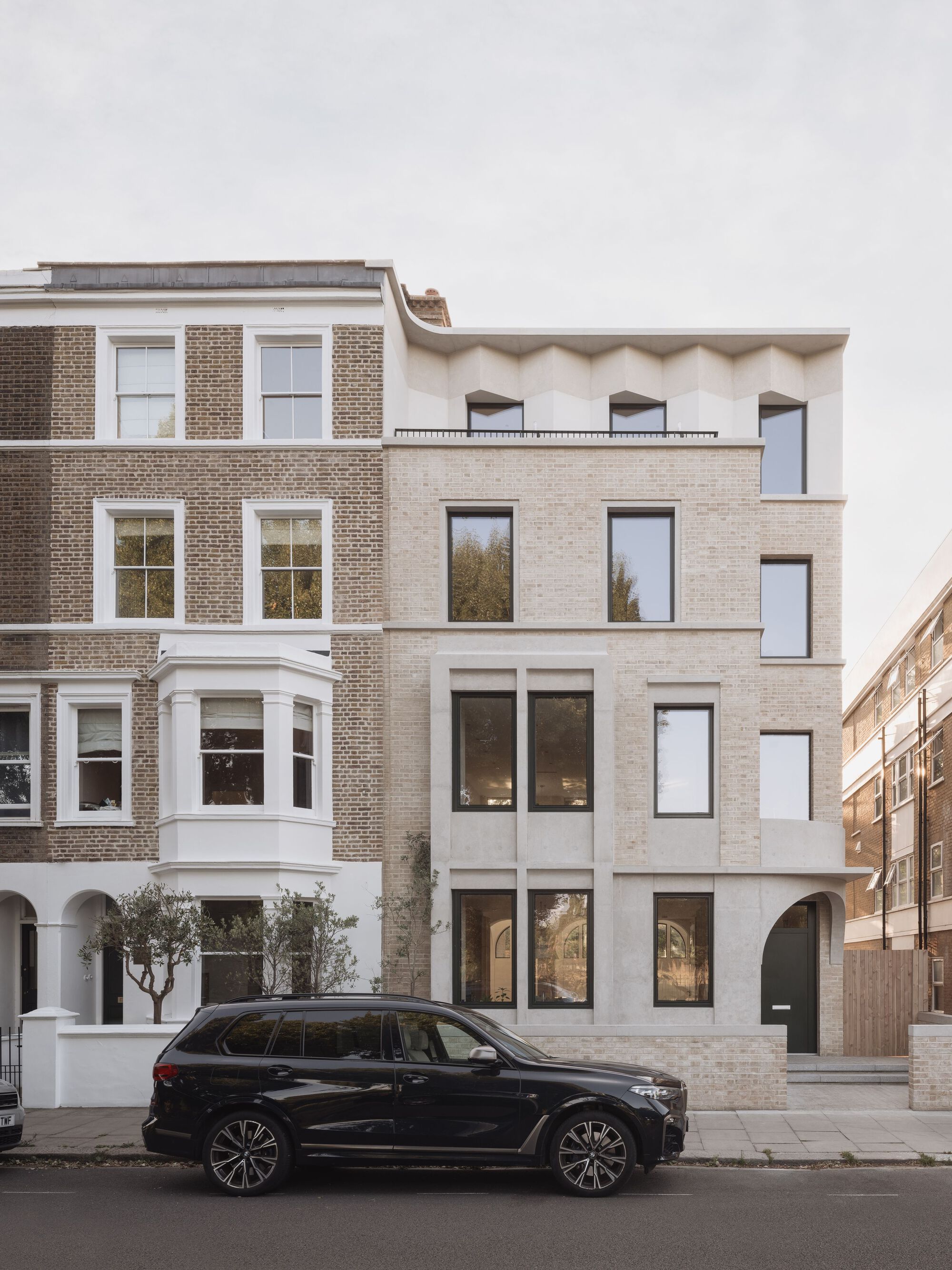 Street facade showing pale brick infill between traditional brick rowhouses with a parked car in front