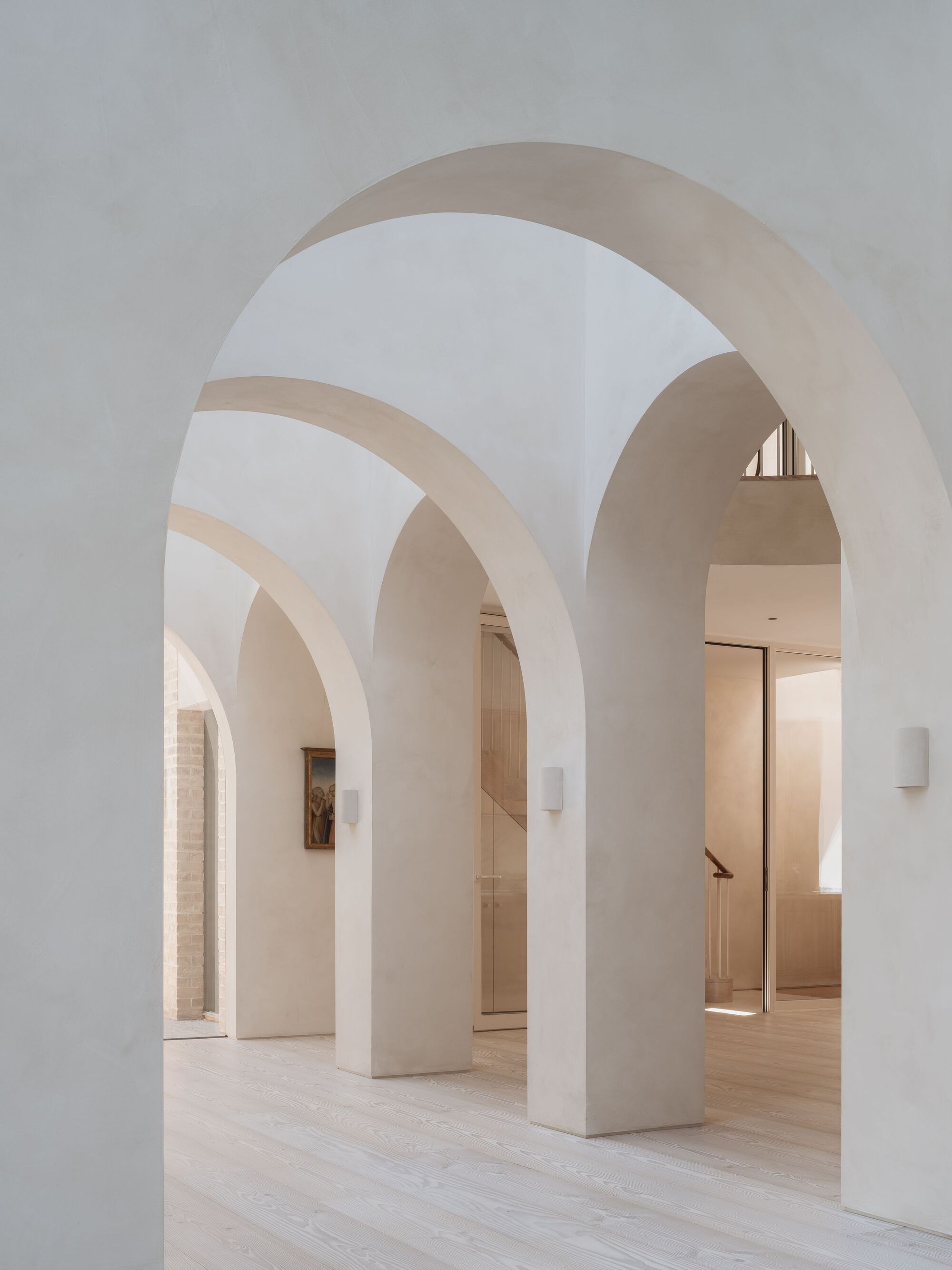 Sequence of arched openings framing interior rooms with pale plaster and timber flooring