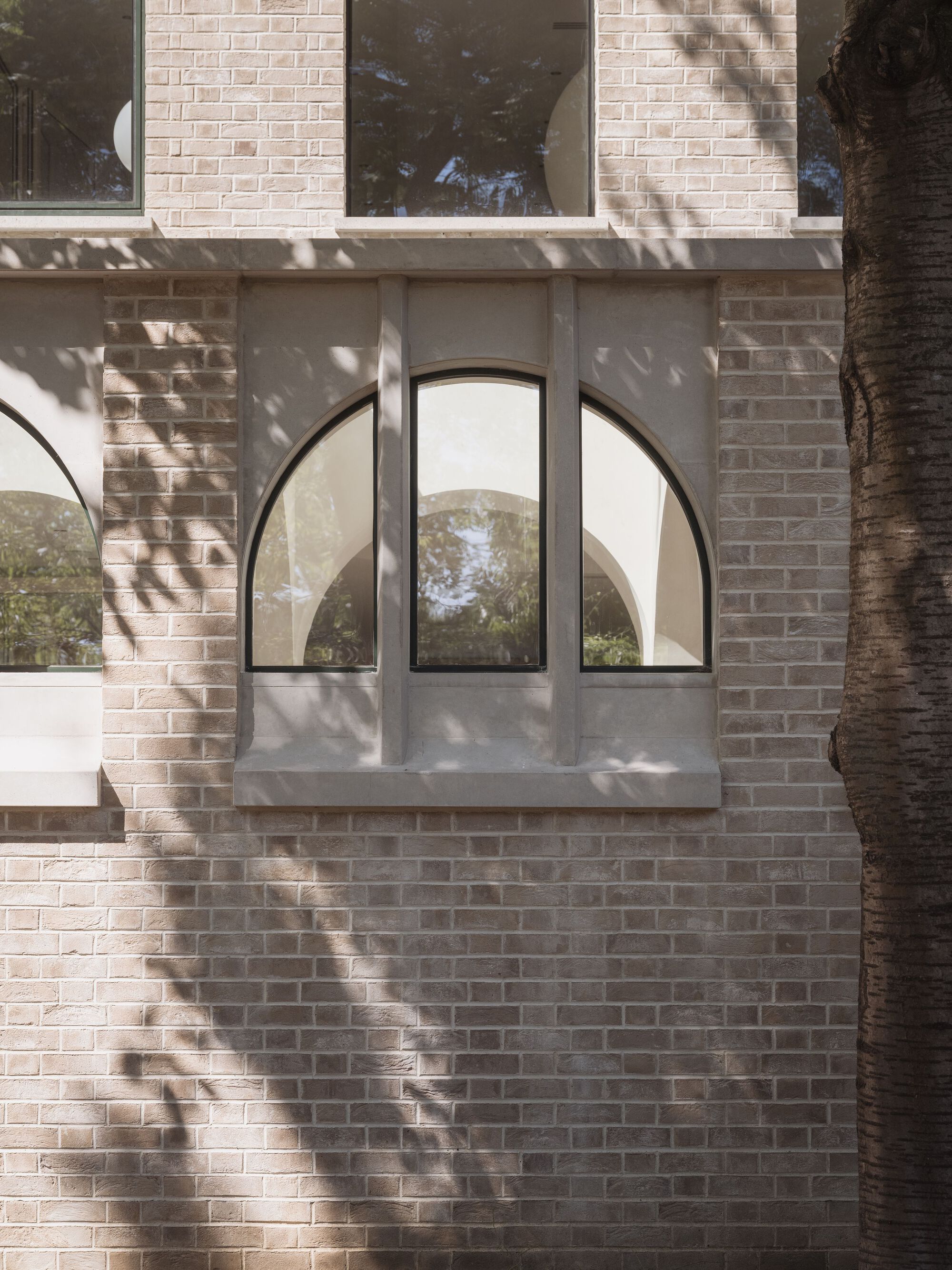 Arched window with steel frames set in pale brick with dappled tree shadows across the wall