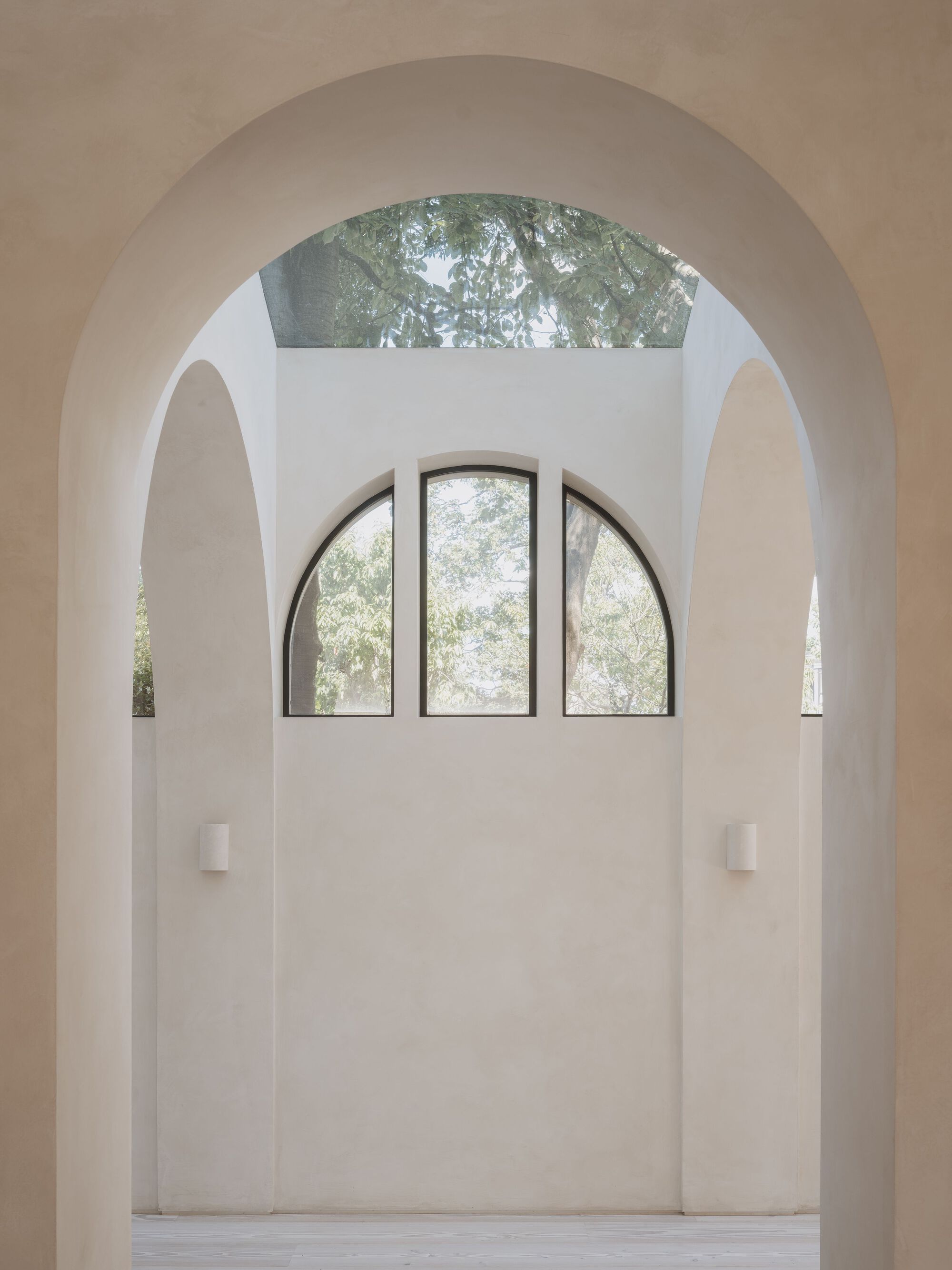 Arched window framed within layered vaulted openings and a skylight above filtering green foliage