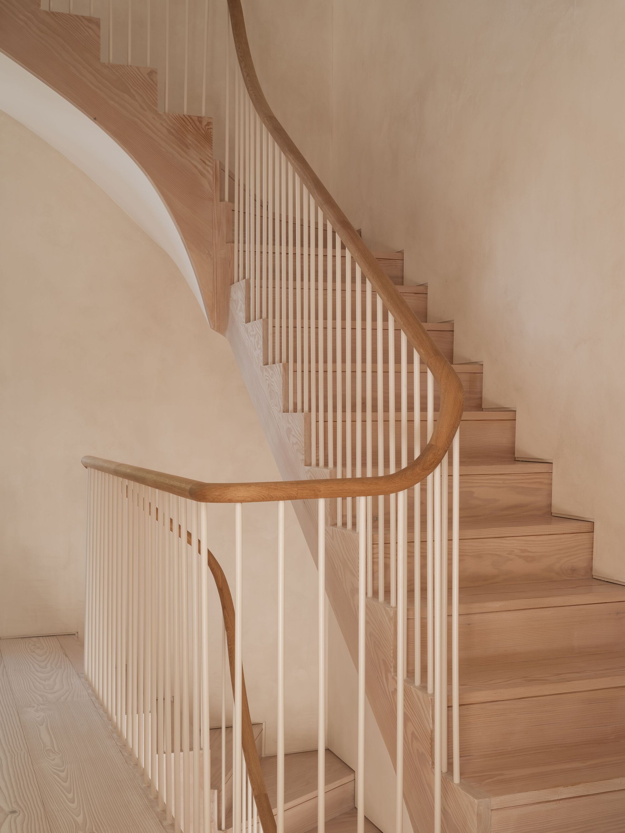 Curved timber staircase with vertical slat balustrade ascending along a smooth plaster wall
