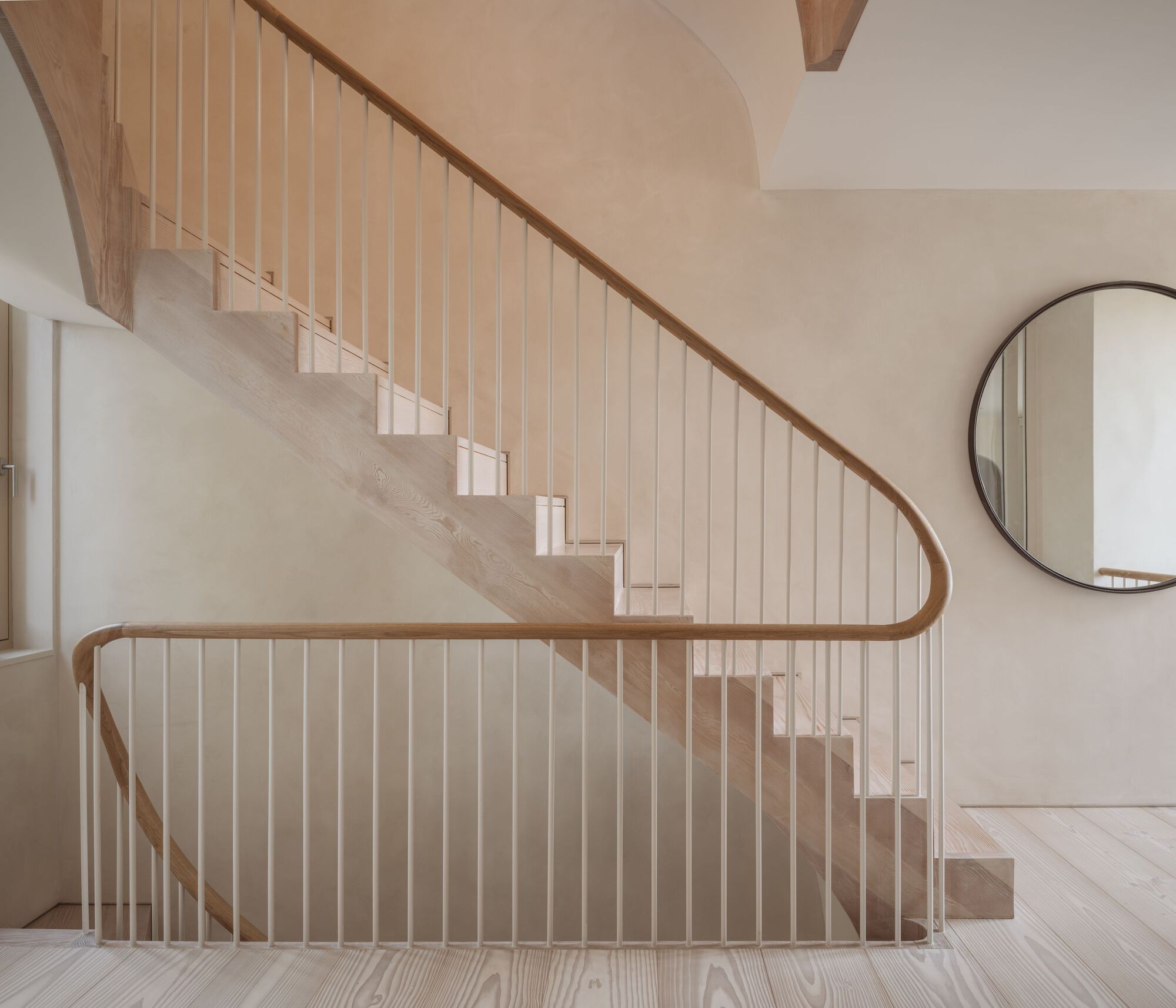 Timber staircase with curved handrail and vertical balusters beneath a vaulted plaster ceiling