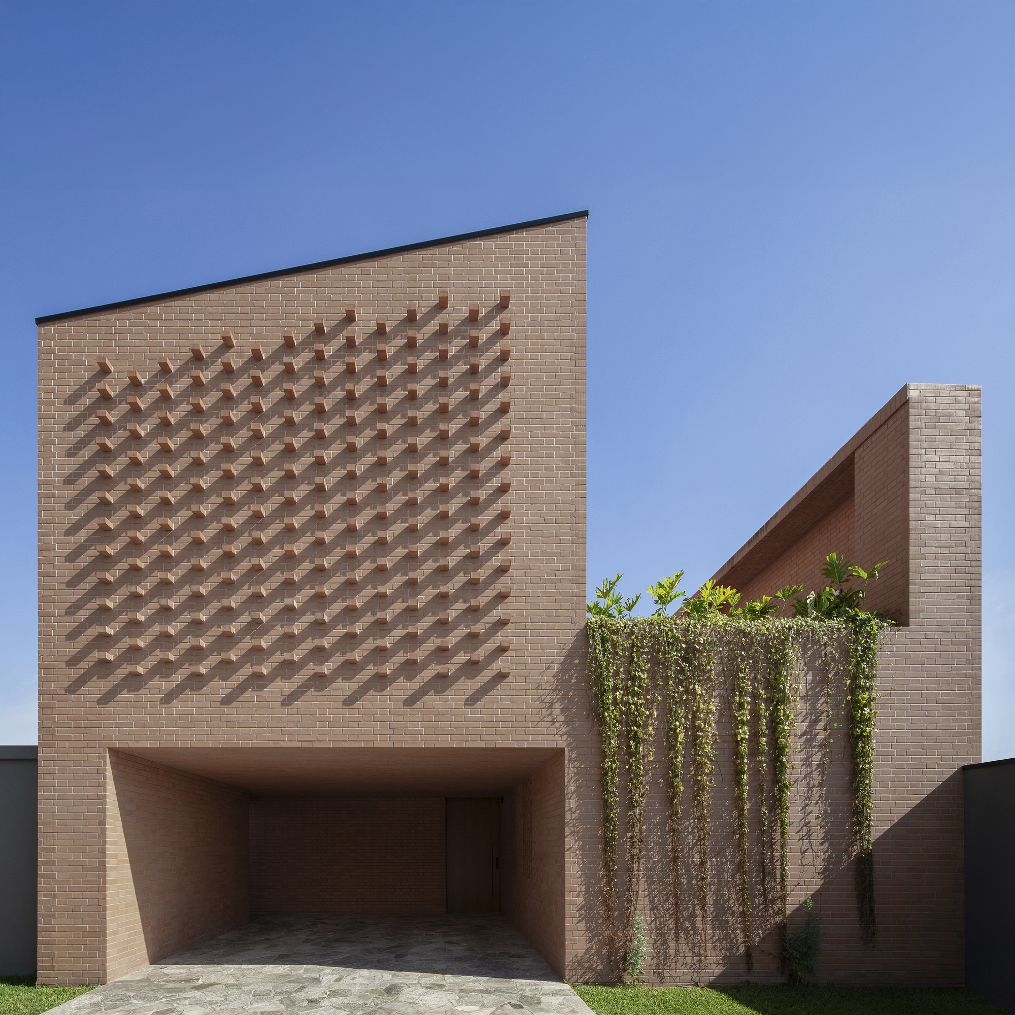 Street facade with protruding brick chevron pattern above a recessed garage and cascading vines at the corner