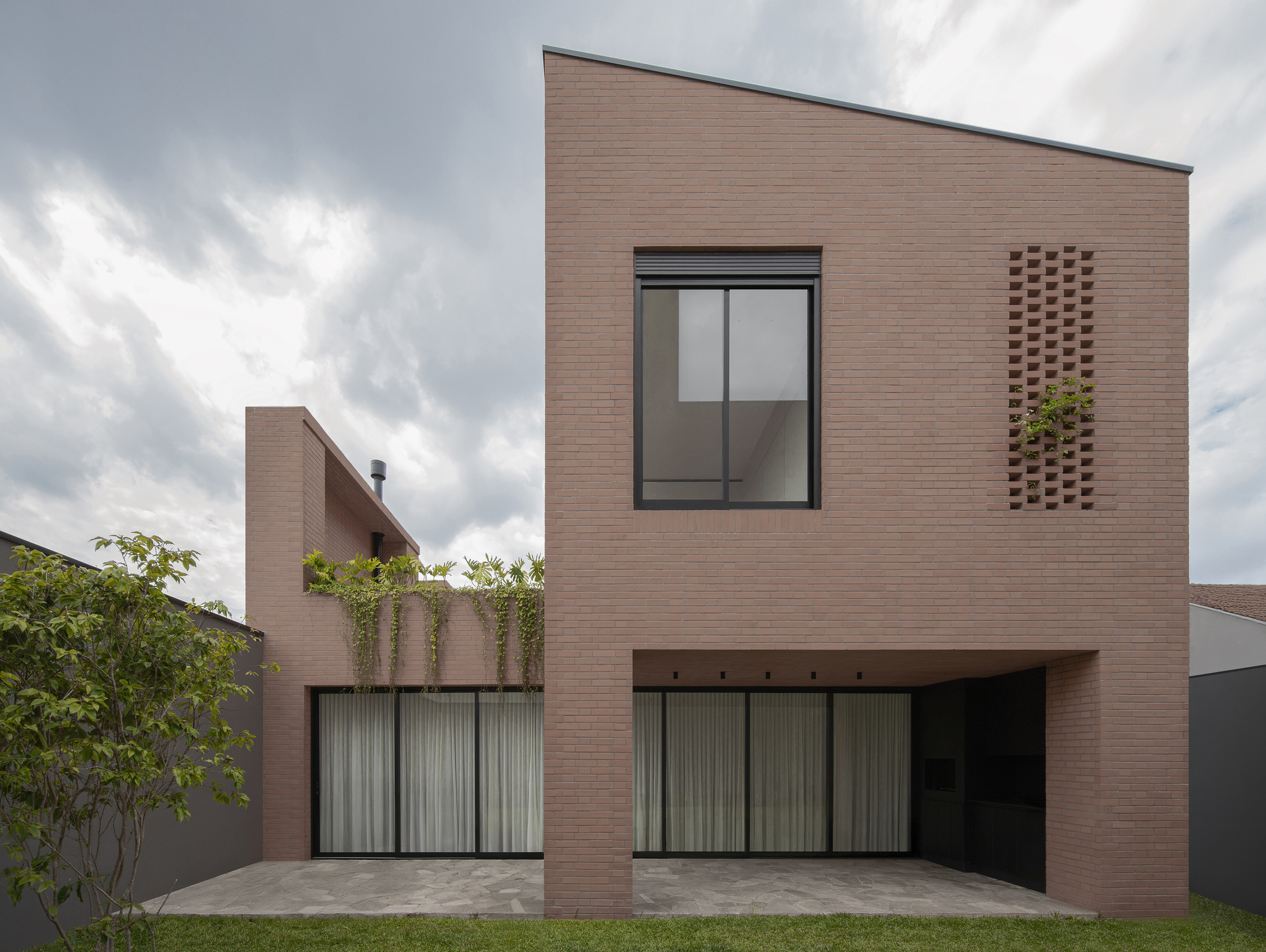Two-storey brick elevation with staggered window openings and perforated brick ventilation panel under cloudy sky