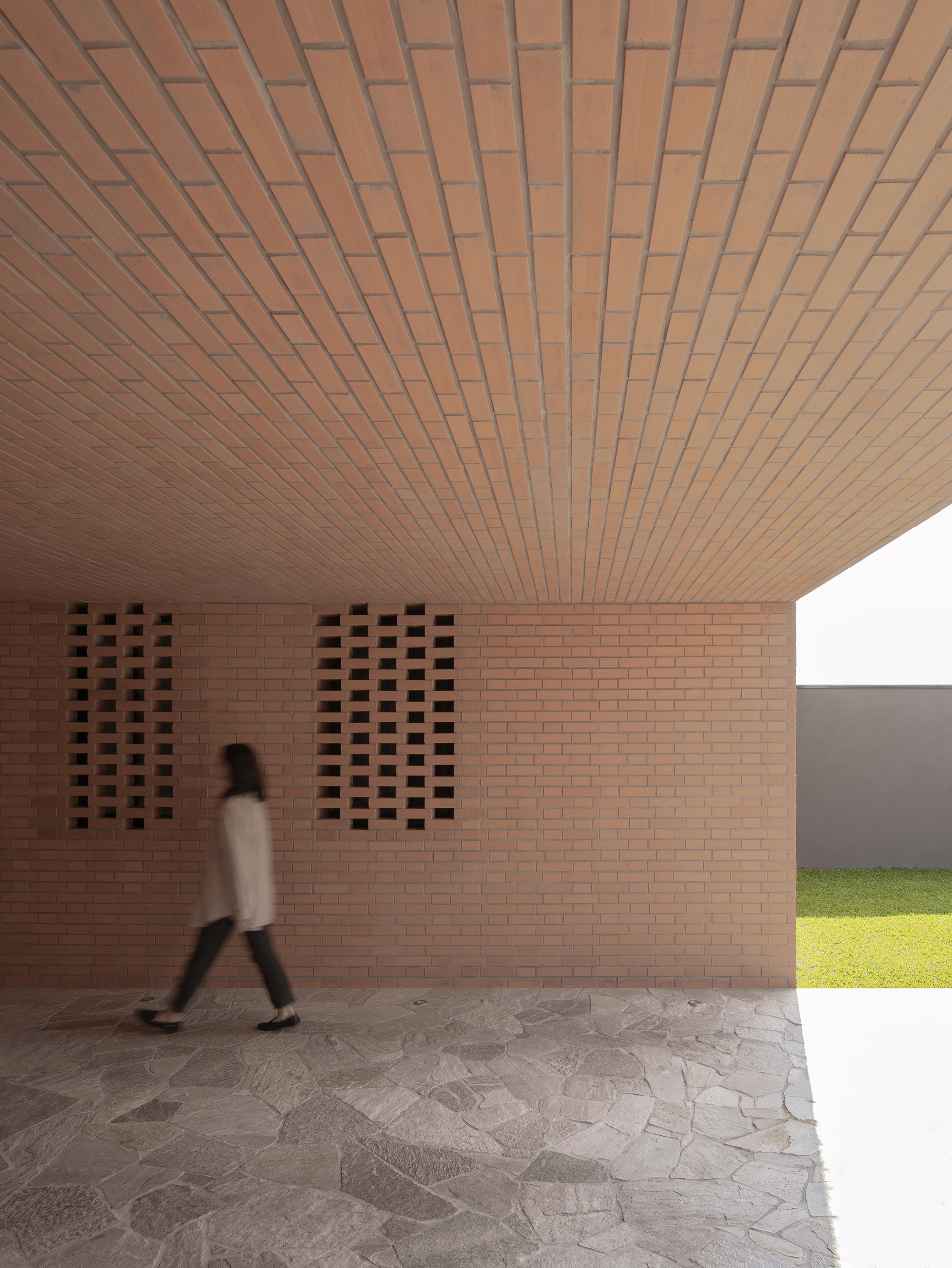 Covered entry passage with brick ceiling and perforated wall panels as a figure walks through