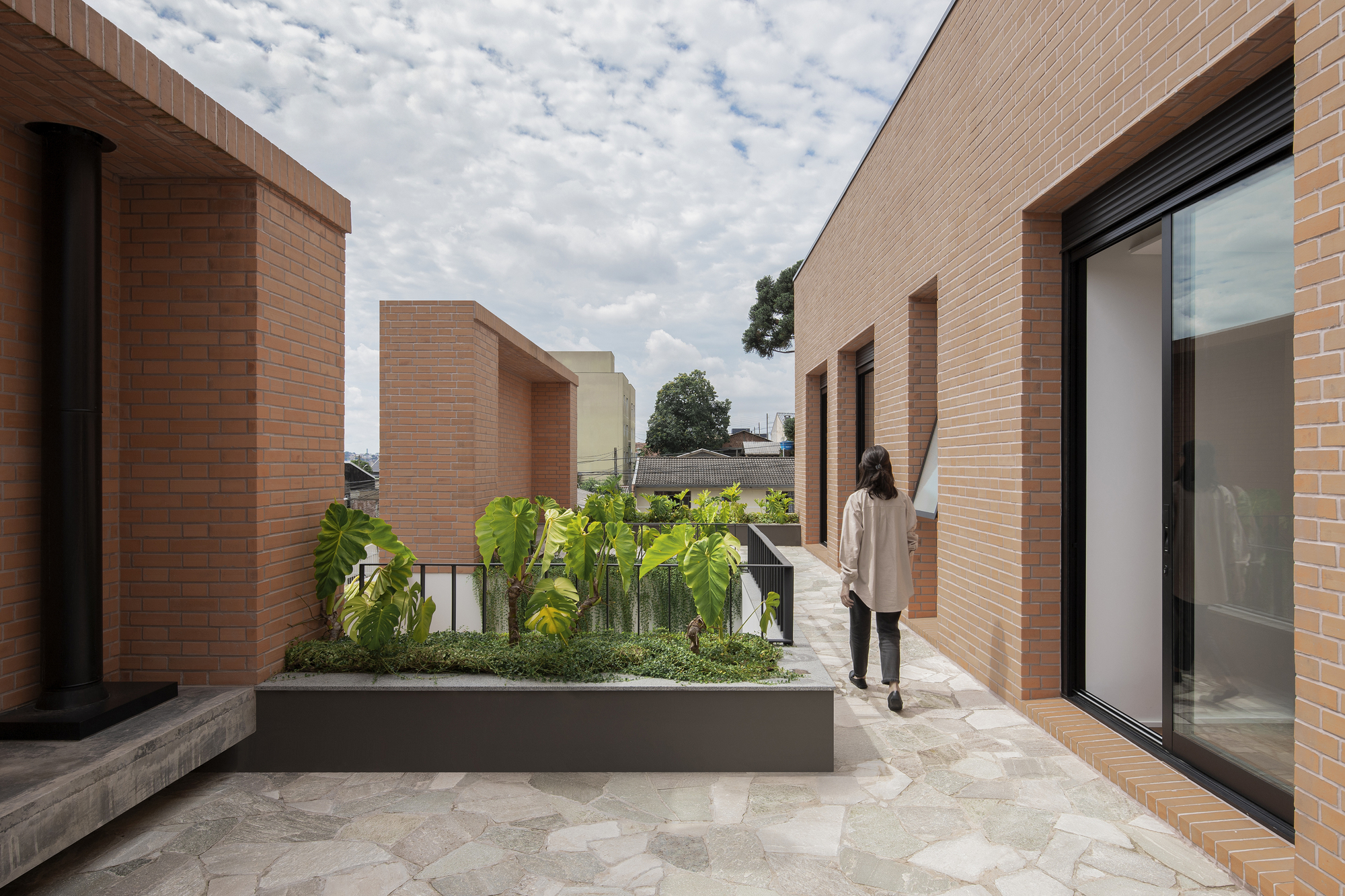 Rooftop terrace with raised planting beds and brick volumes framing views under a cloudy sky