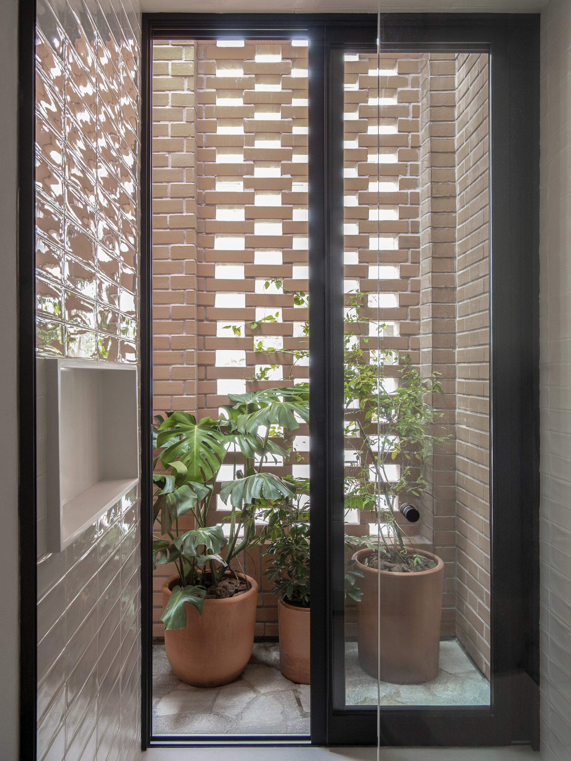 Interior view through glass door to narrow courtyard with perforated brick screen and potted plants