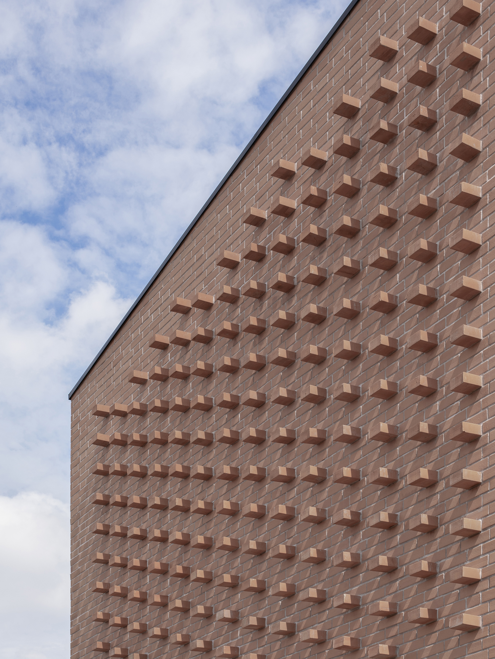 Angled view of brick facade with grid of protruding brick elements against scattered clouds