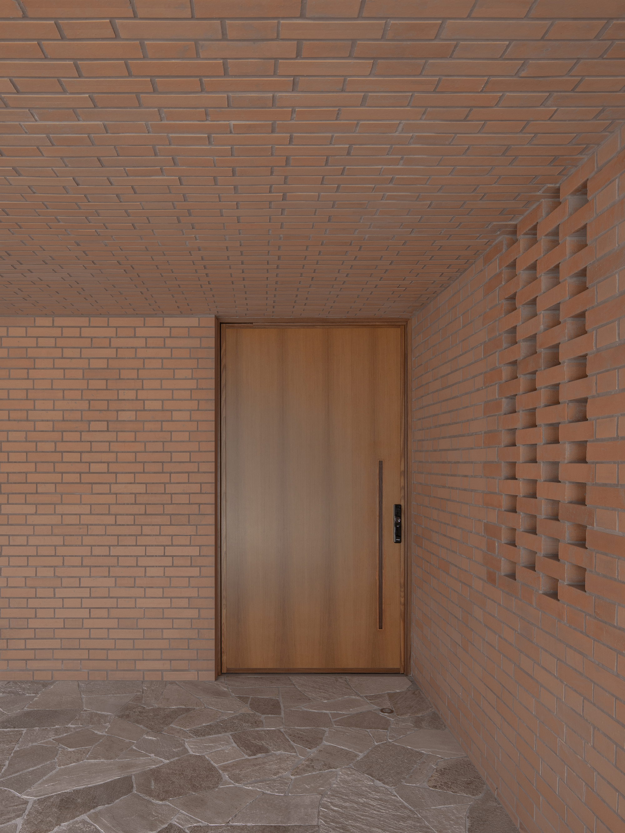 Entry vestibule with timber door flanked by flat and textured brick walls under brick ceiling