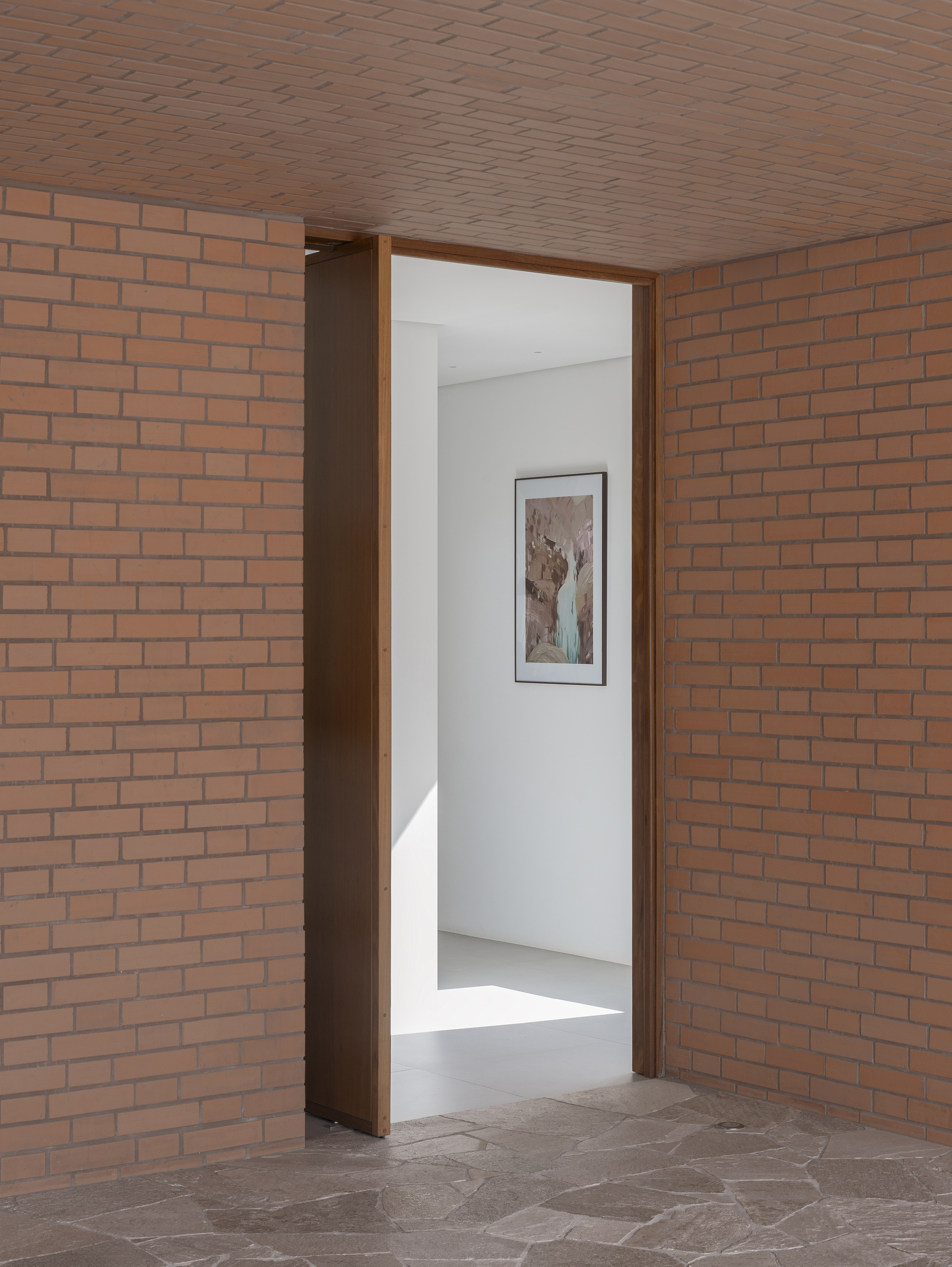 Brick corridor leading through a doorway to a white gallery space with artwork on the wall