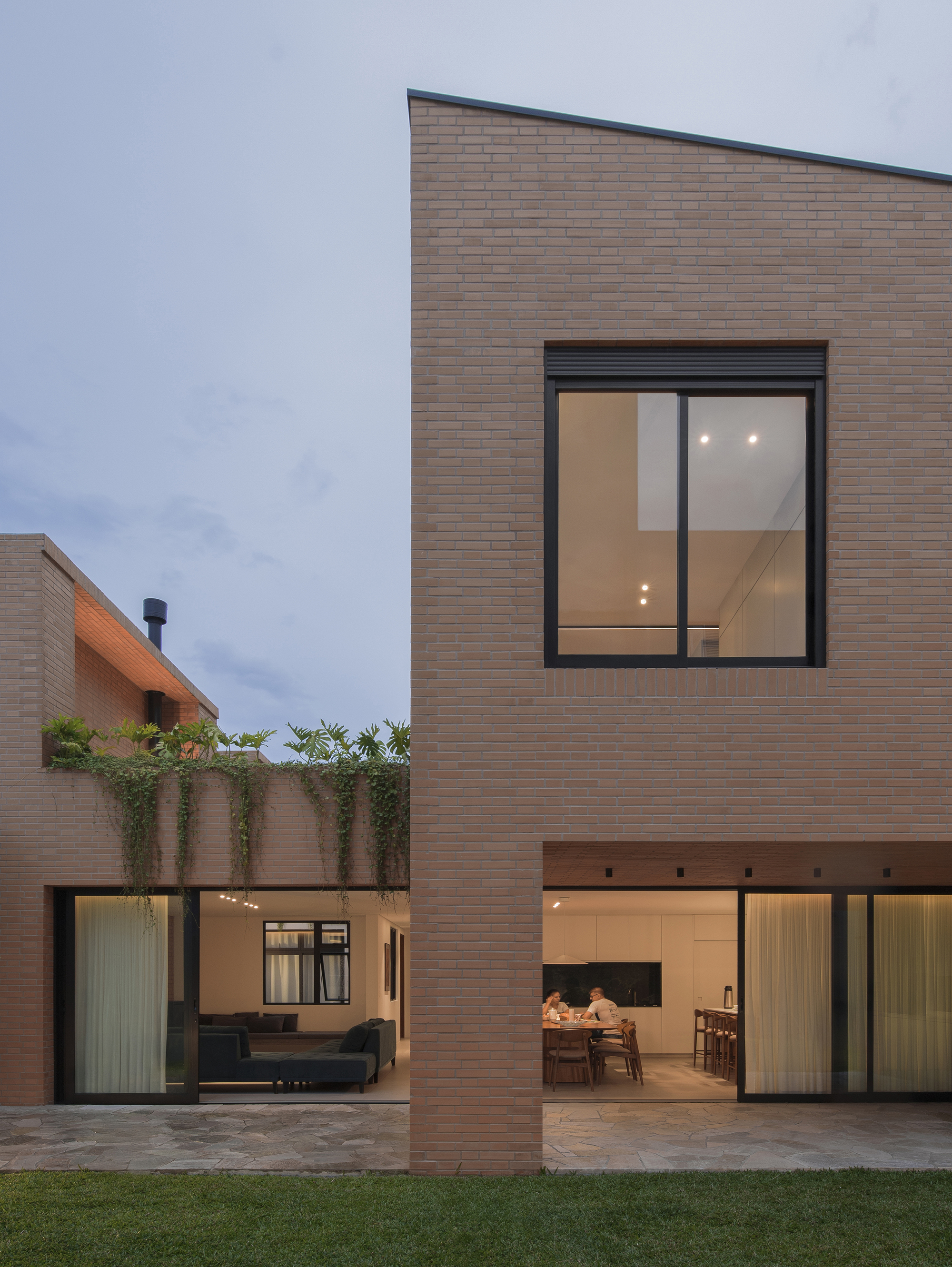 Two-story brick residence with glazed openings and courtyard at dusk