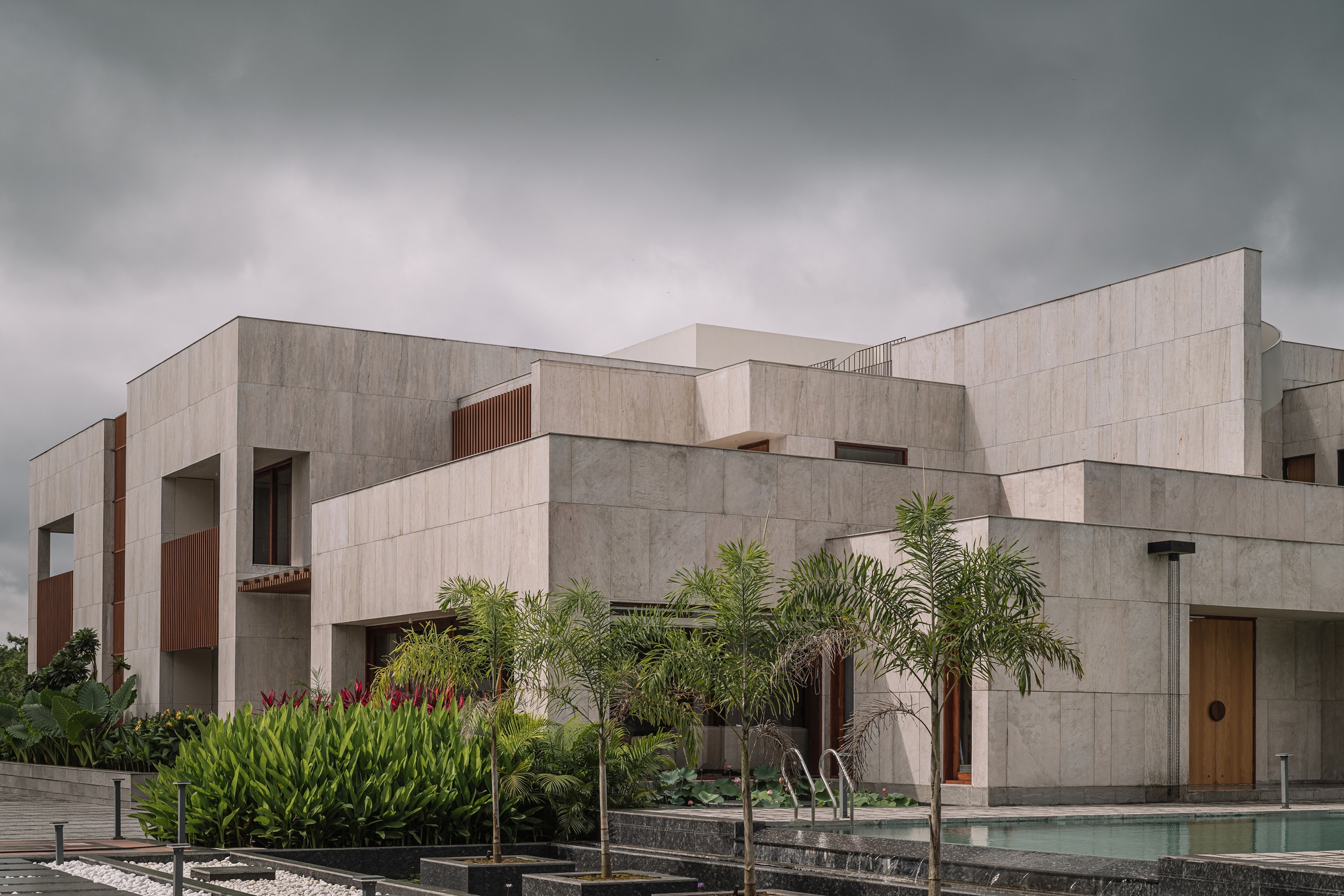 Rear facade with stacked concrete volumes overlooking a pool with palms and tropical plantings