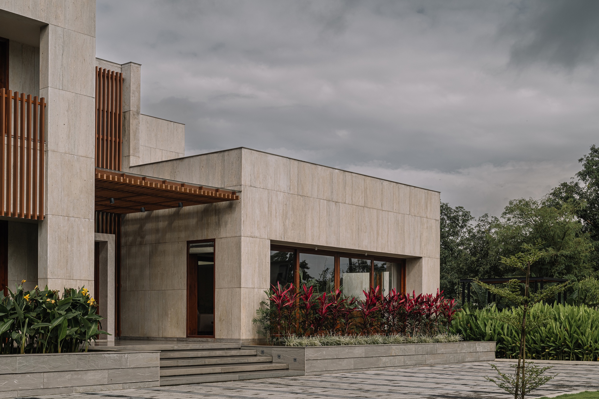 Limestone panel facade with timber screens and planted beds under an overcast sky