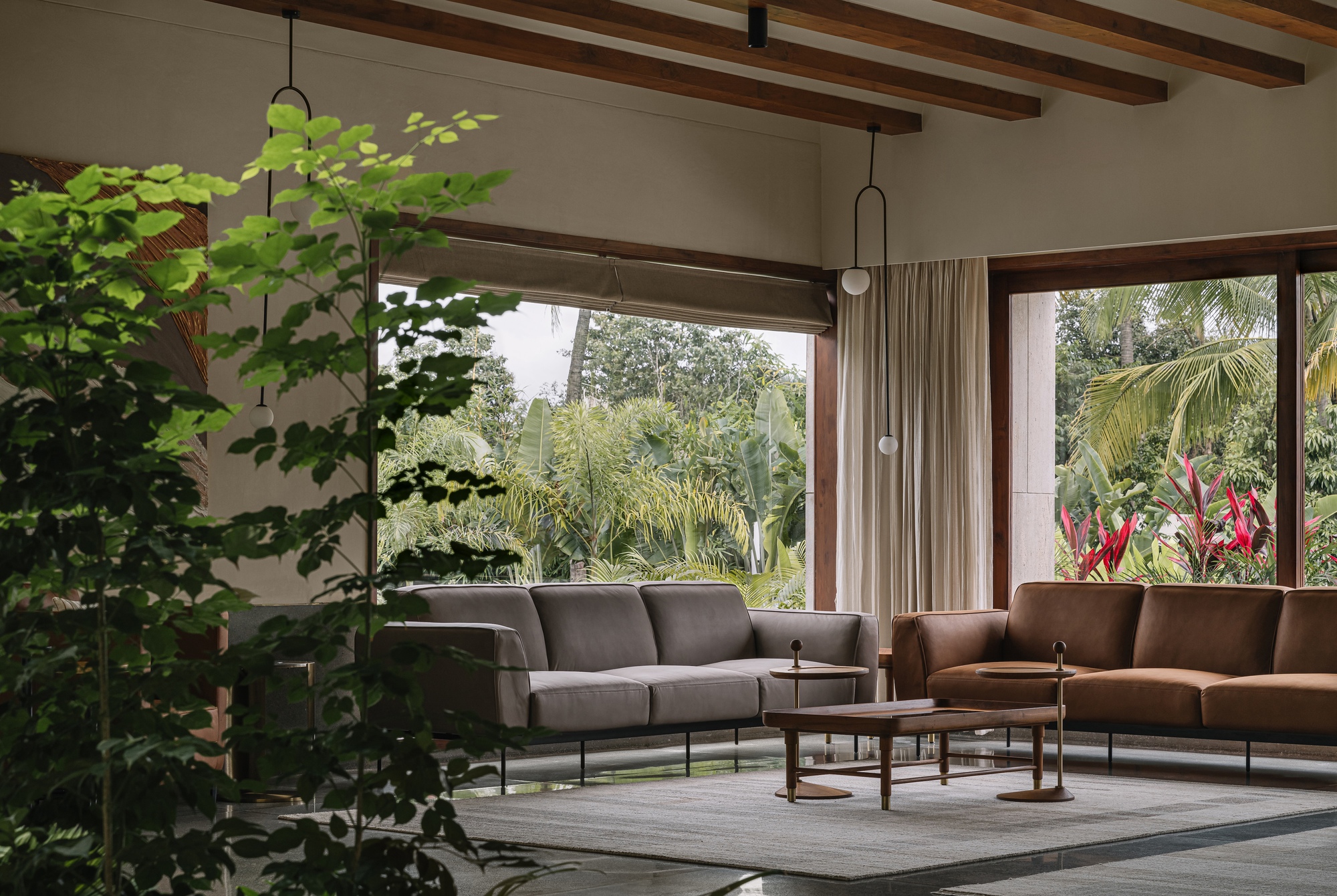 Living room with exposed timber beams and floor-to-ceiling windows overlooking tropical planting
