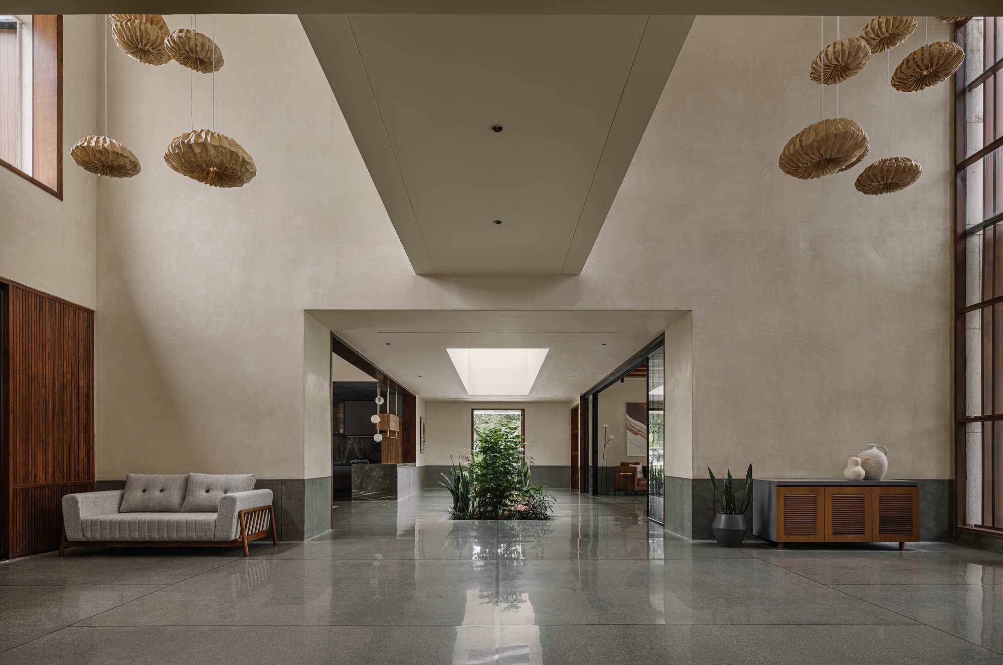 Double-height entry hall with polished grey floor, woven pendant lights, and planted interior courtyard beyond