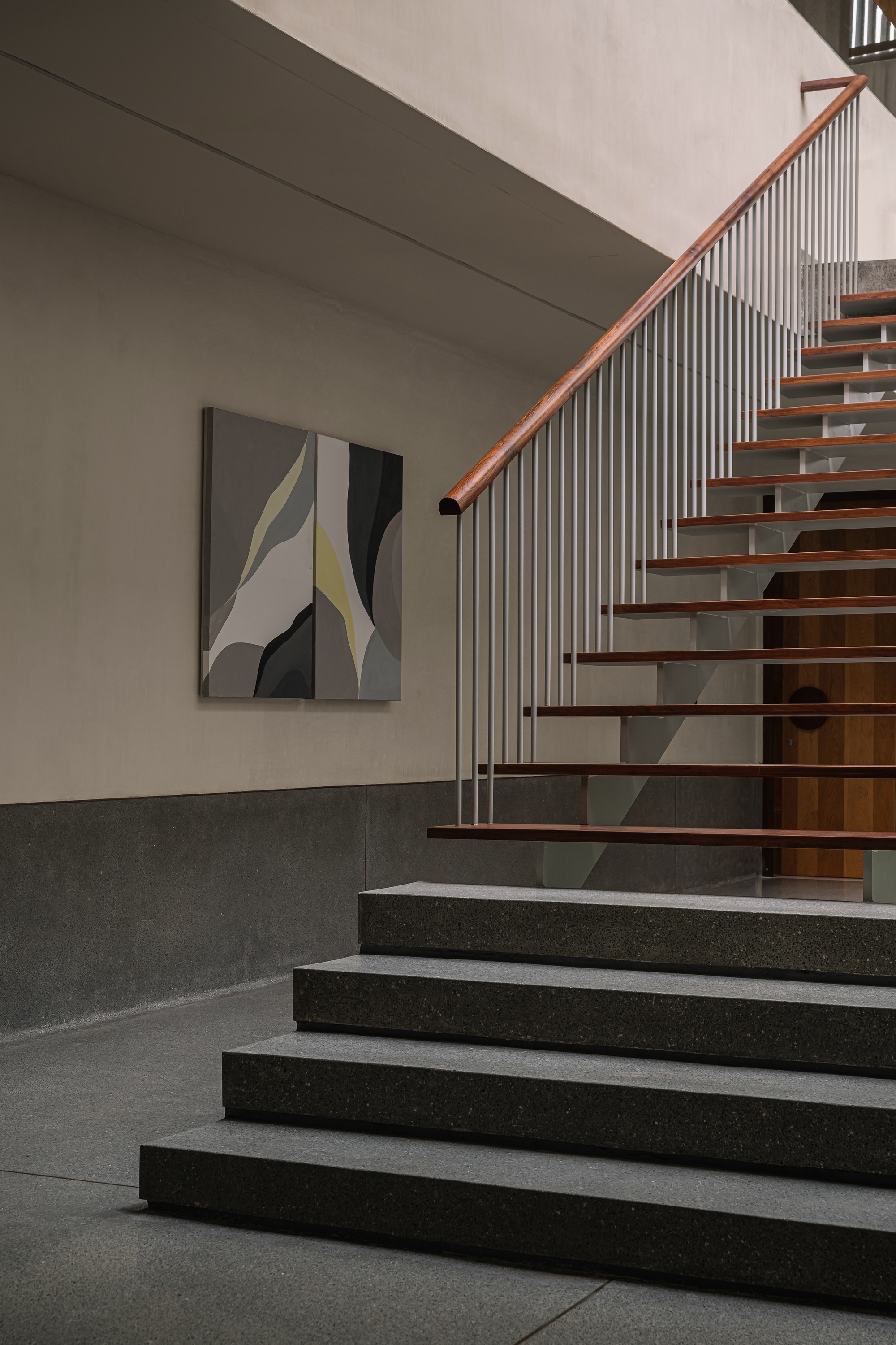Detail of timber-tread staircase with vertical metal balusters and timber handrail against two-tone wall