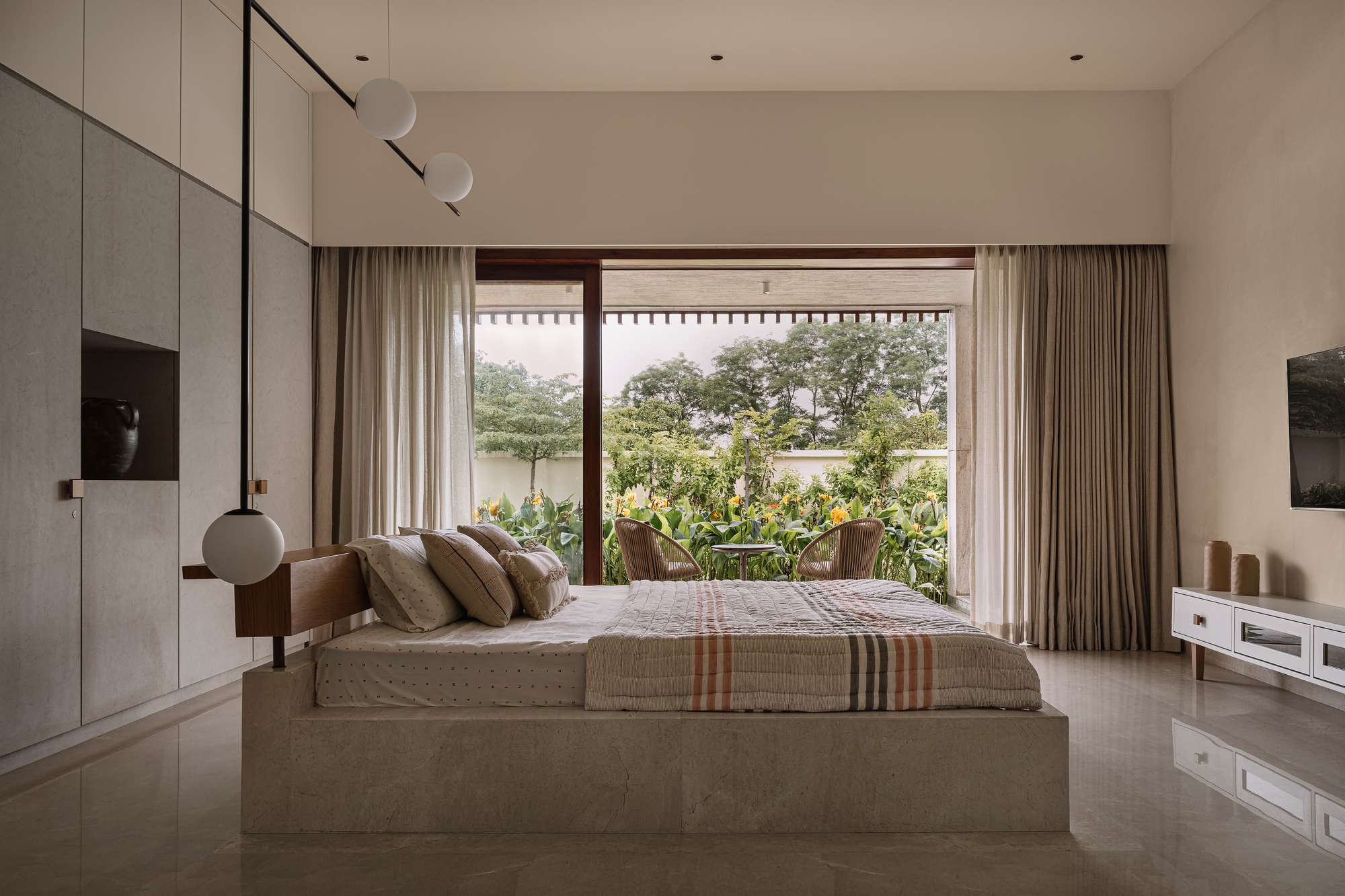 Bedroom interior with terrazzo platform bed facing garden view through sliding glass doors