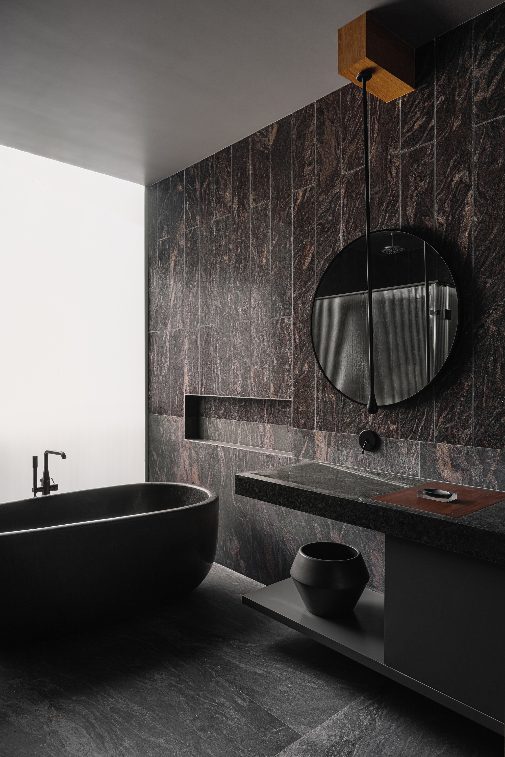 Bathroom with dark marble wall tiles, black freestanding tub and floating vanity with round mirror