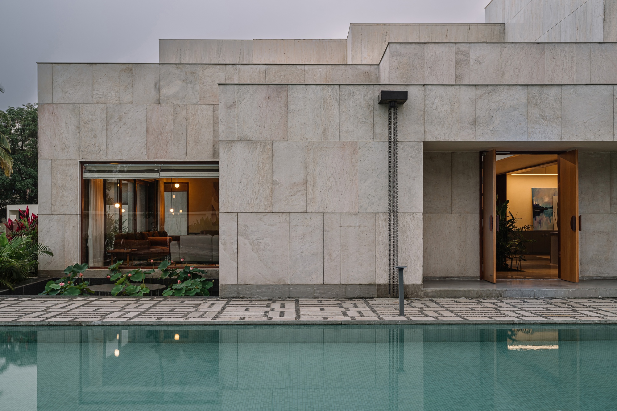 Limestone facade with stepped volumes reflected in a still swimming pool at dusk