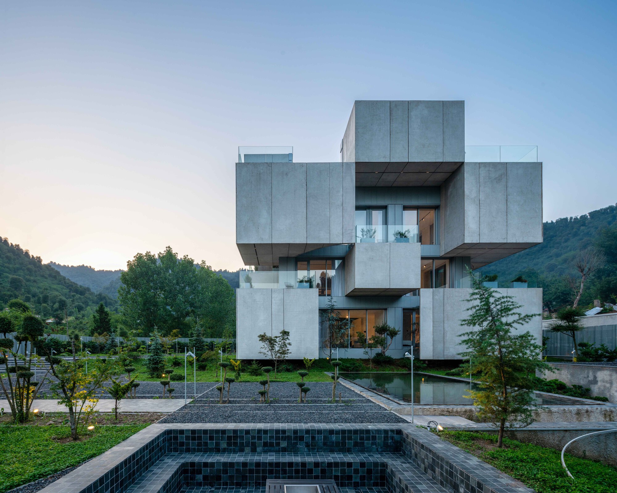 Rear facade showing concrete volumes above a dark-tiled reflecting pool with trees and hillside beyond