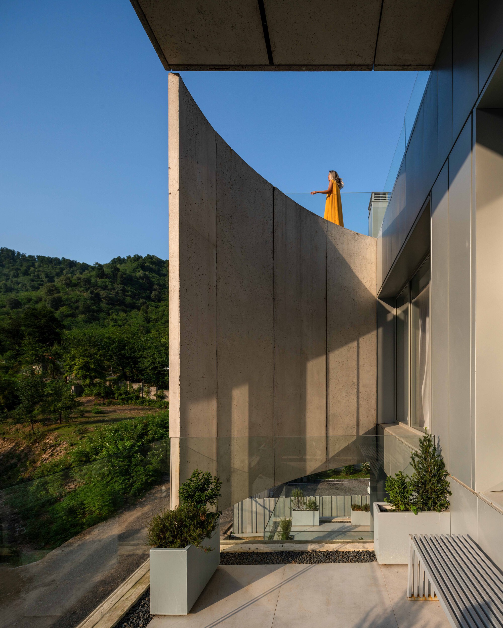 Upper terrace with curved concrete wall and planted beds overlooking forested hills at dusk