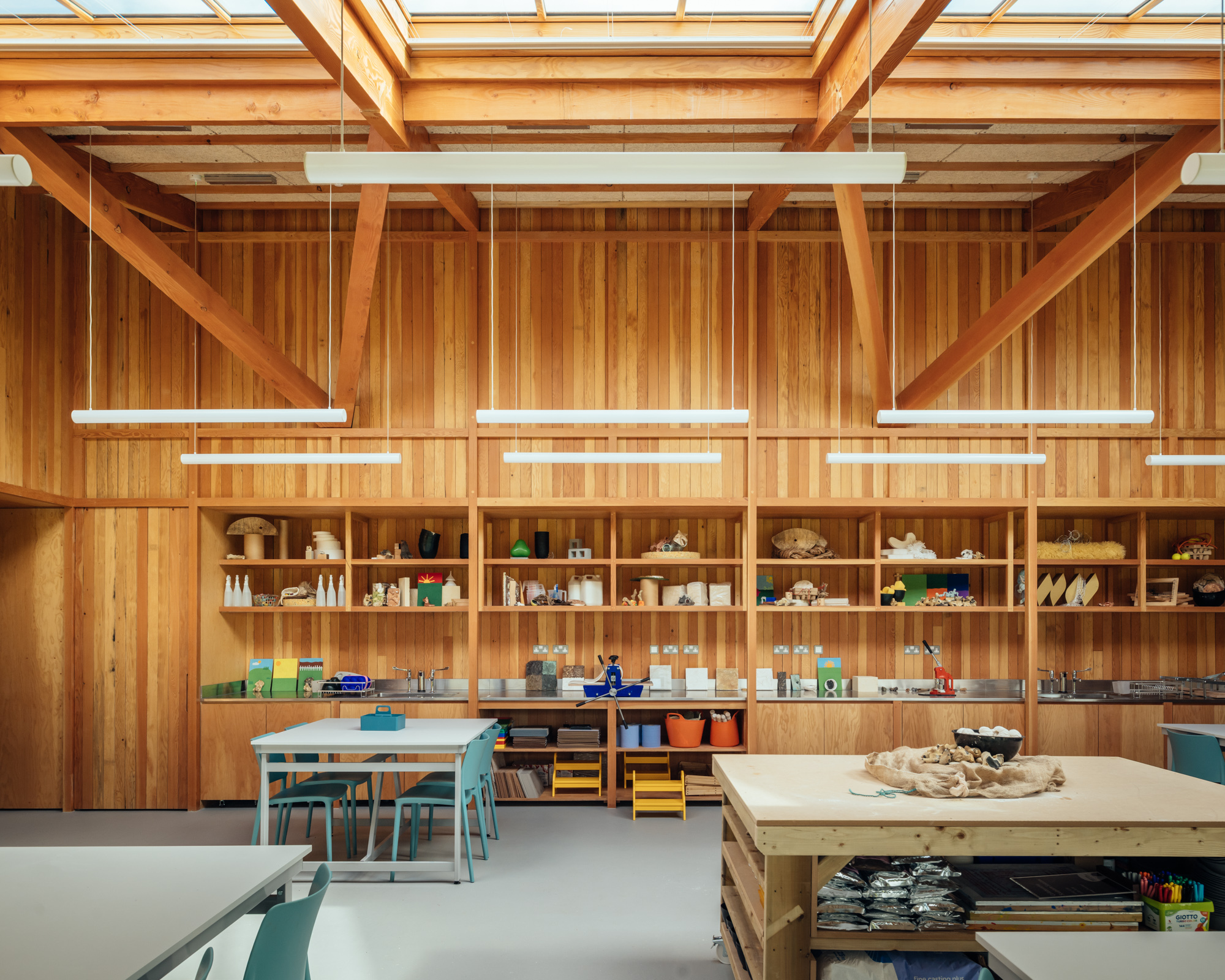 Vertical timber wall with built-in shelving displaying student work beneath suspended linear lighting fixtures