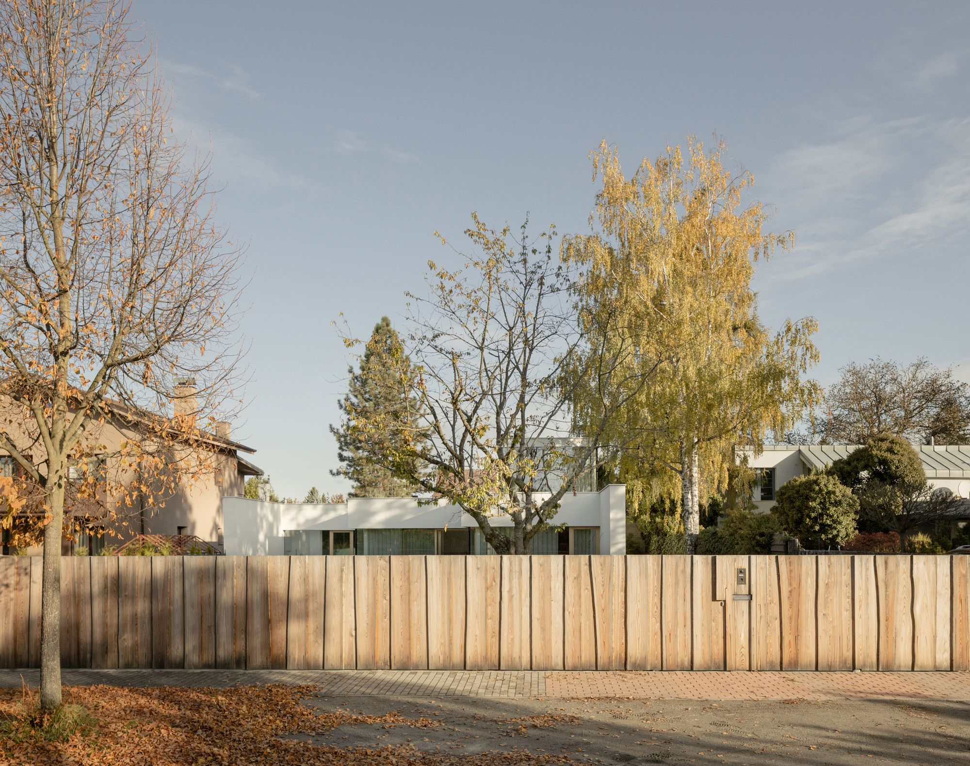 Street view of vertical timber fence screening the residence behind bare and golden autumn trees