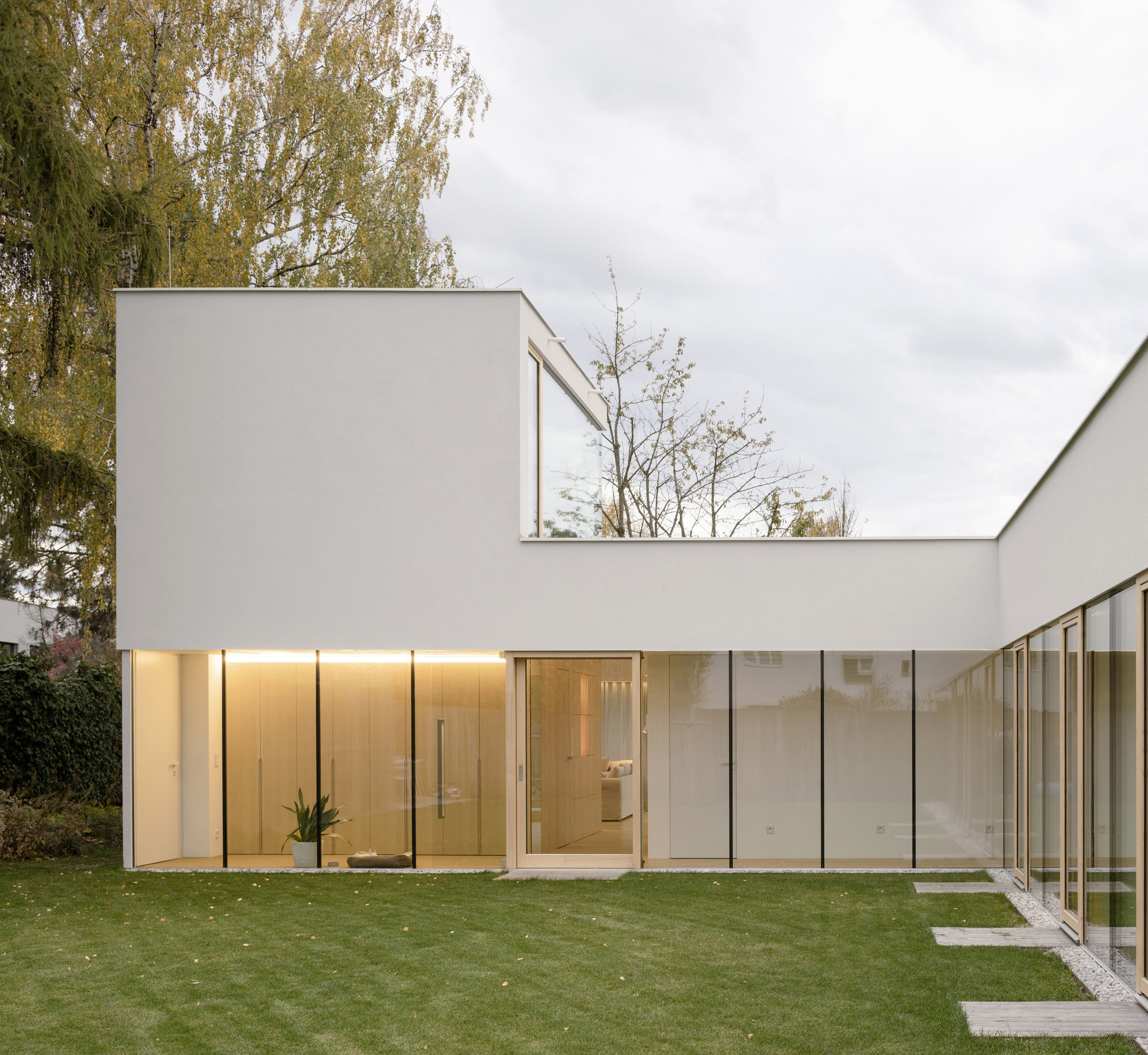 Garden facade with floor-to-ceiling glazing and illuminated timber-clad interior under overcast autumn sky