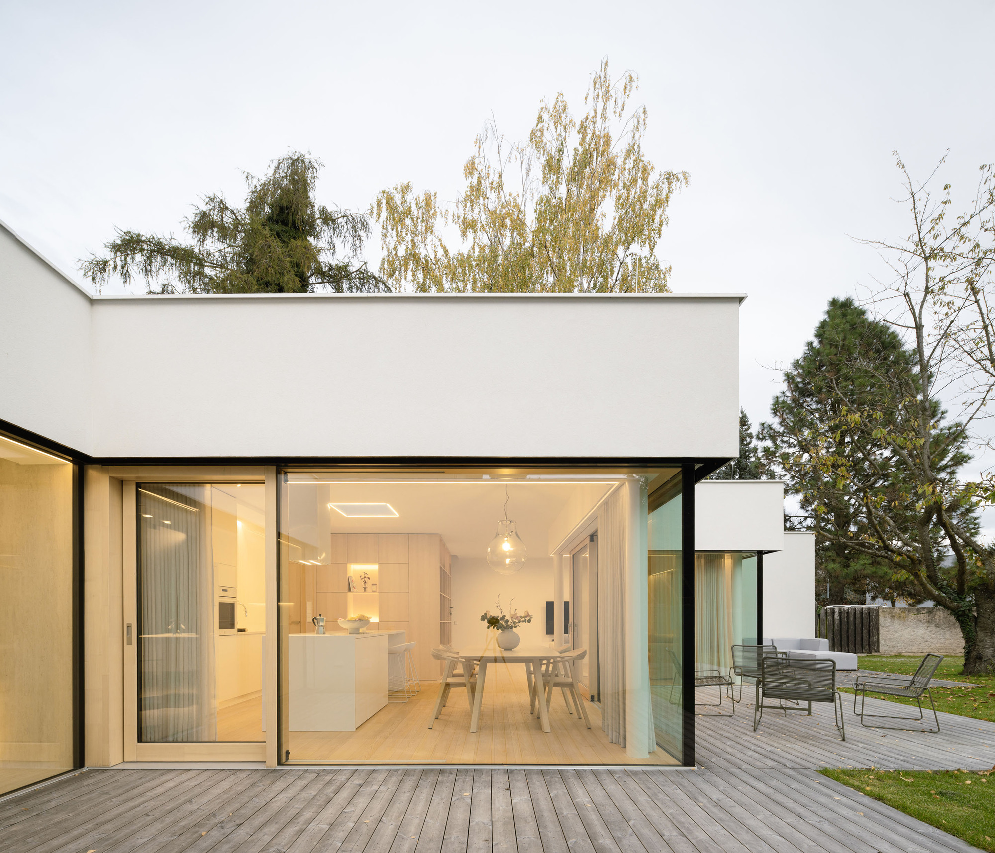 Open sliding glass doors revealing dining area and kitchen from timber deck at dusk