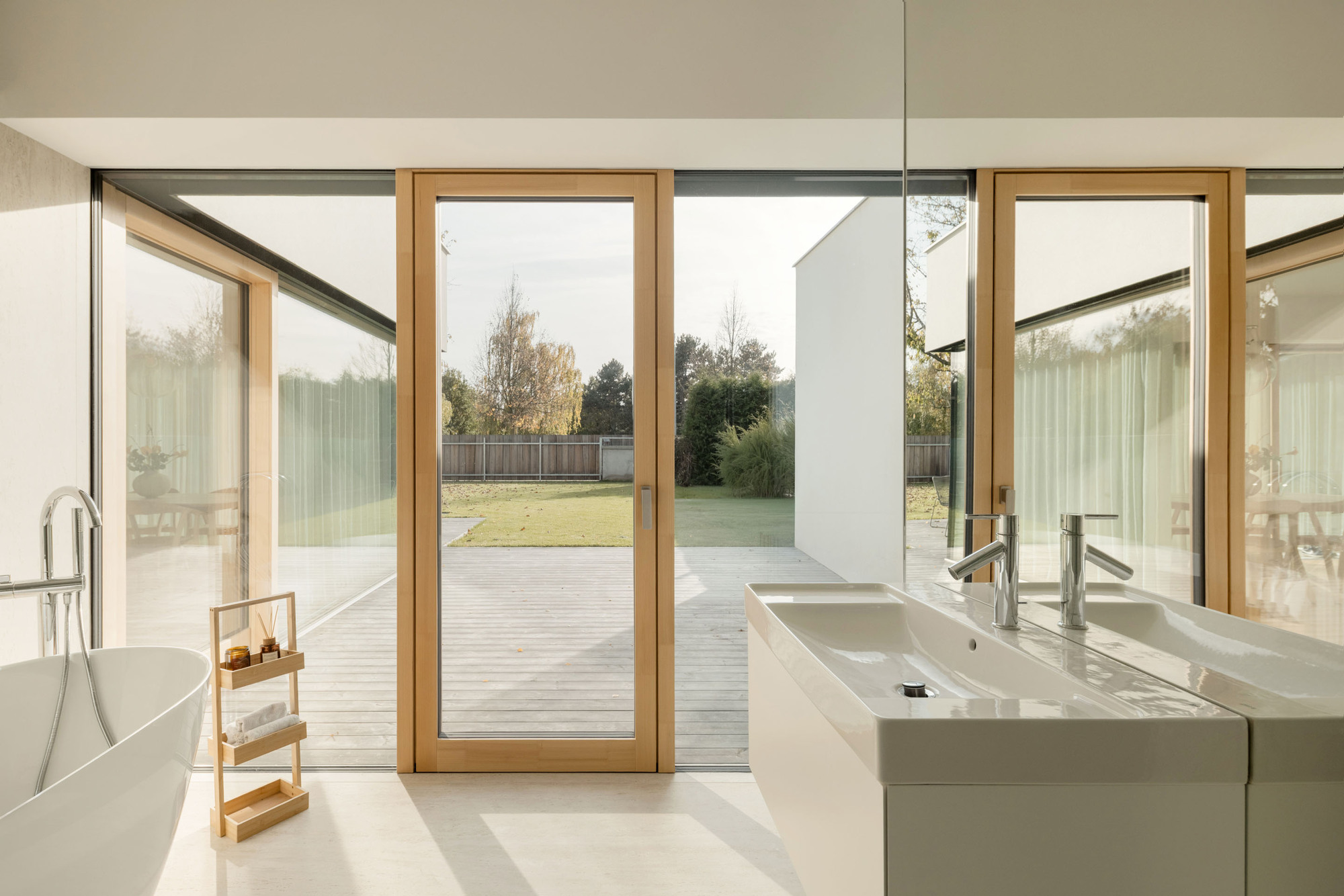 Bathroom with freestanding tub and timber-framed pivot door opening to timber deck and lawn