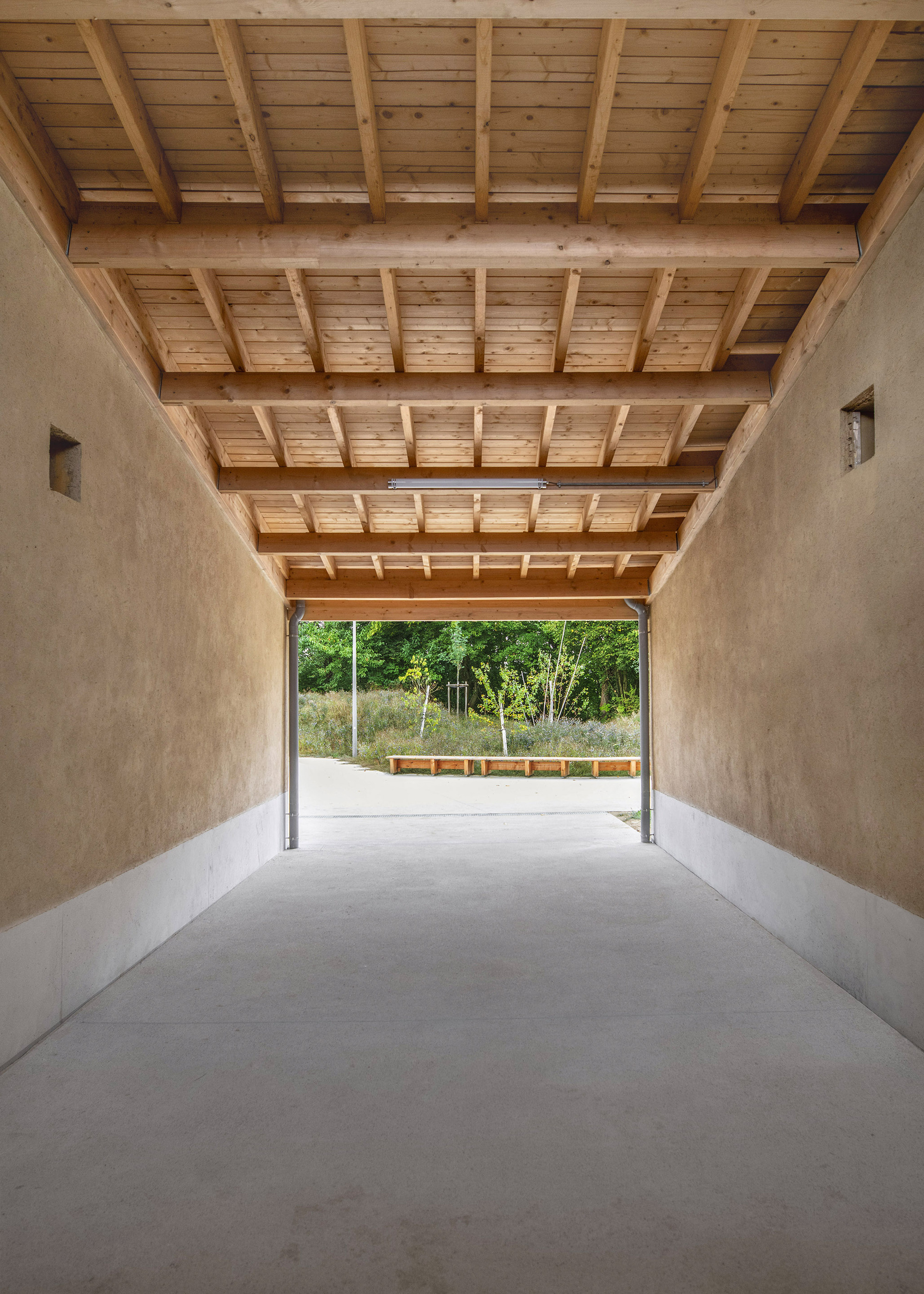 Covered passage with exposed timber joists and beams over polished concrete leading to a garden