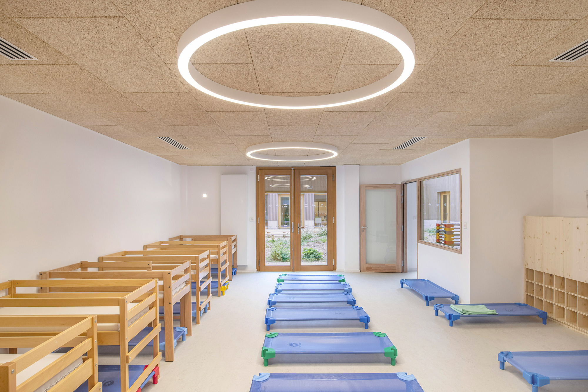 Interior rest room with blue mats on pale floor beneath circular pendant lights and plywood ceiling
