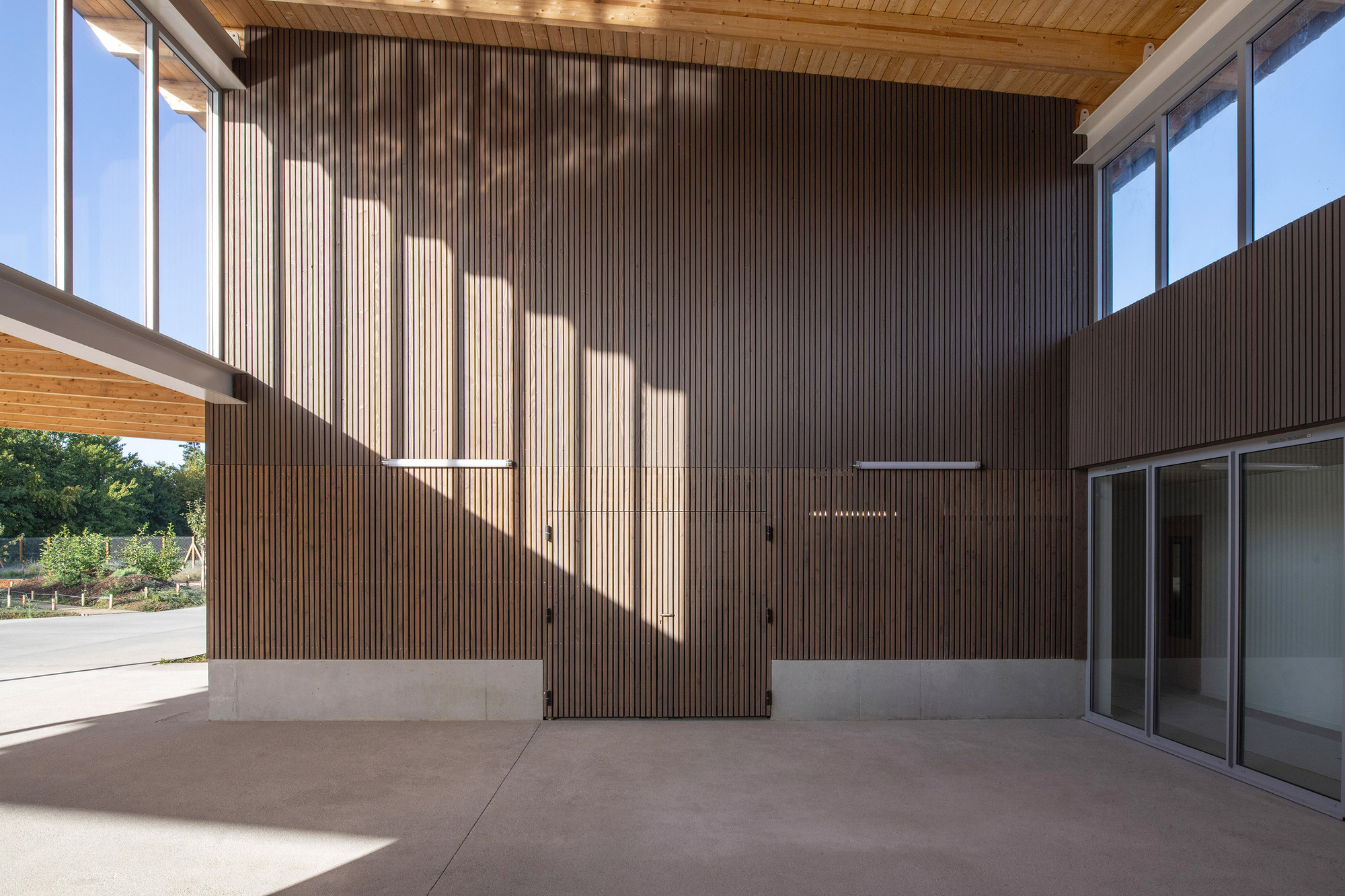 Covered porch with vertical timber slat walls and timber ceiling under angular sunlight shadows