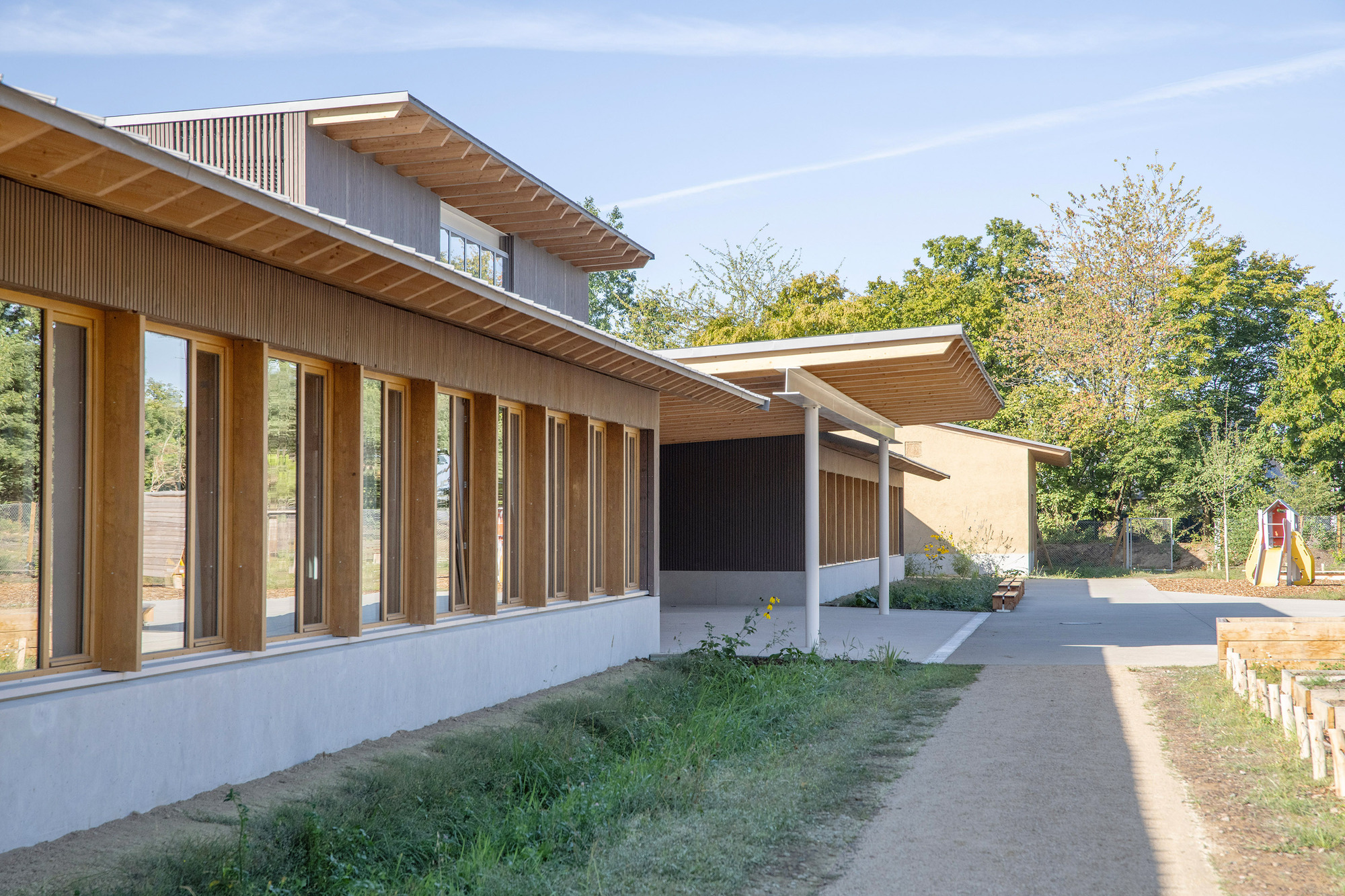 Long view of linked volumes with deep timber eaves and vertical fin facades amid autumn trees