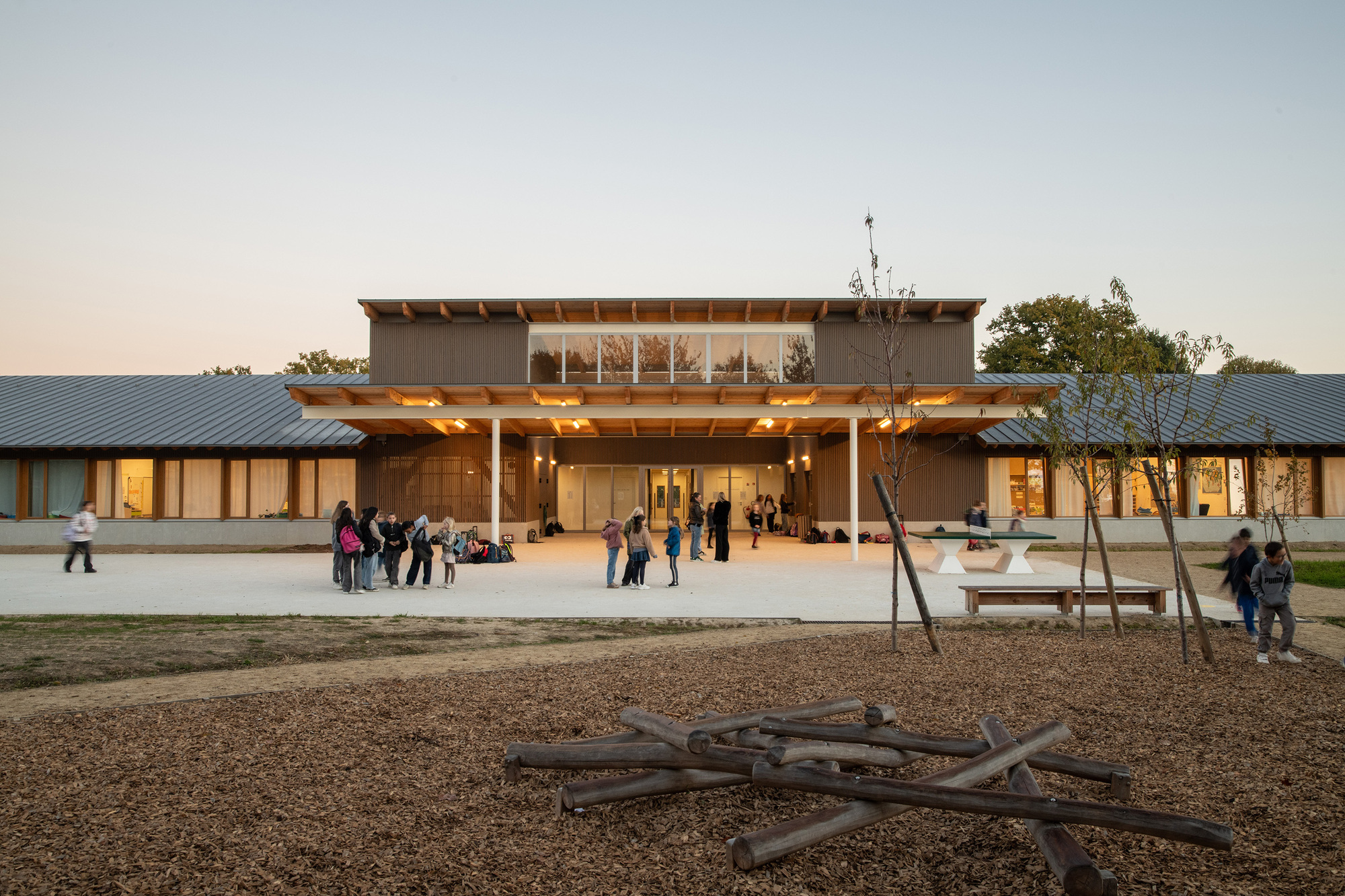 Evening view of the central two-story volume with glazed upper floor and people gathering at dusk