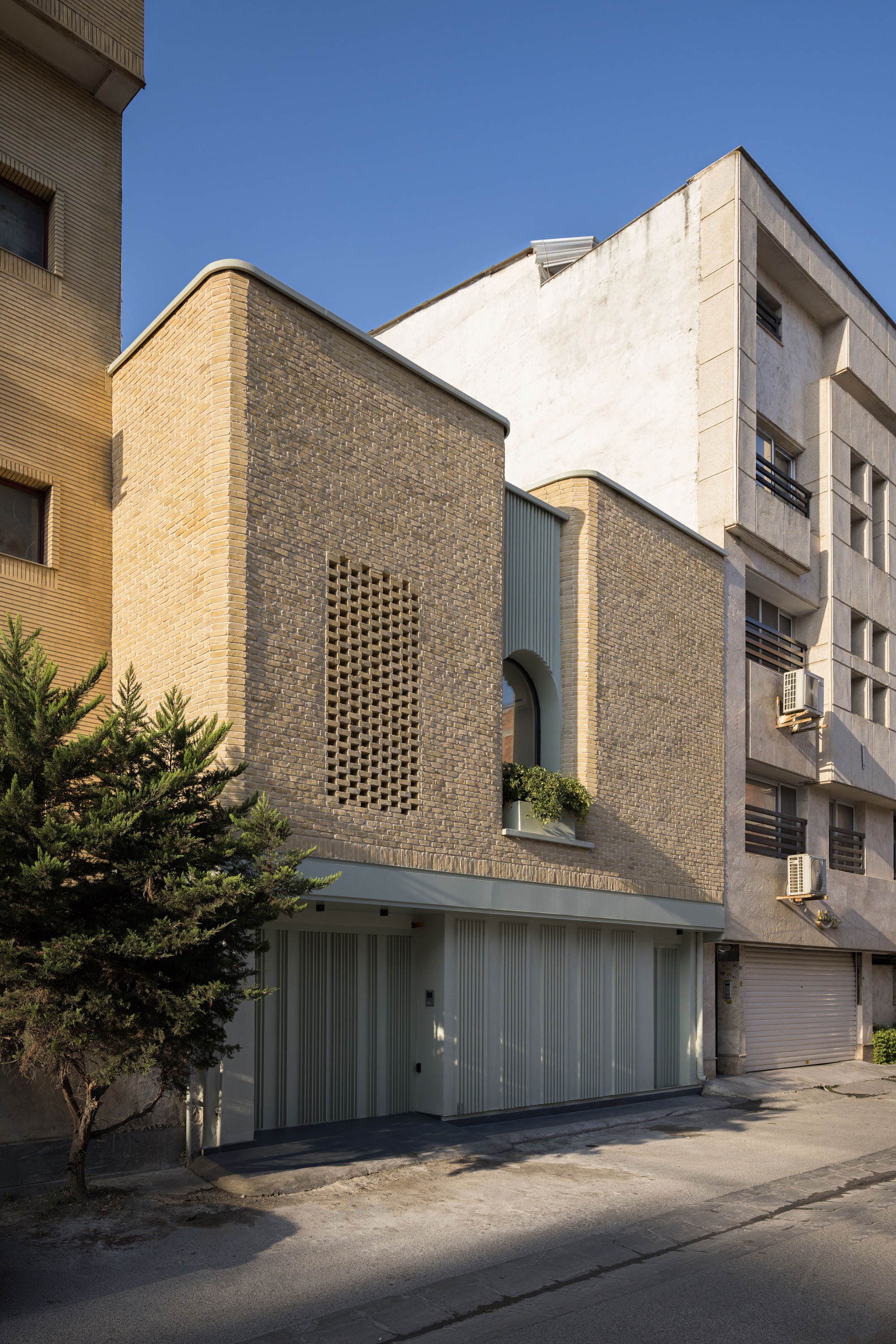 Daylight view of the curved brick facade with twin arched openings and corrugated metal garage below