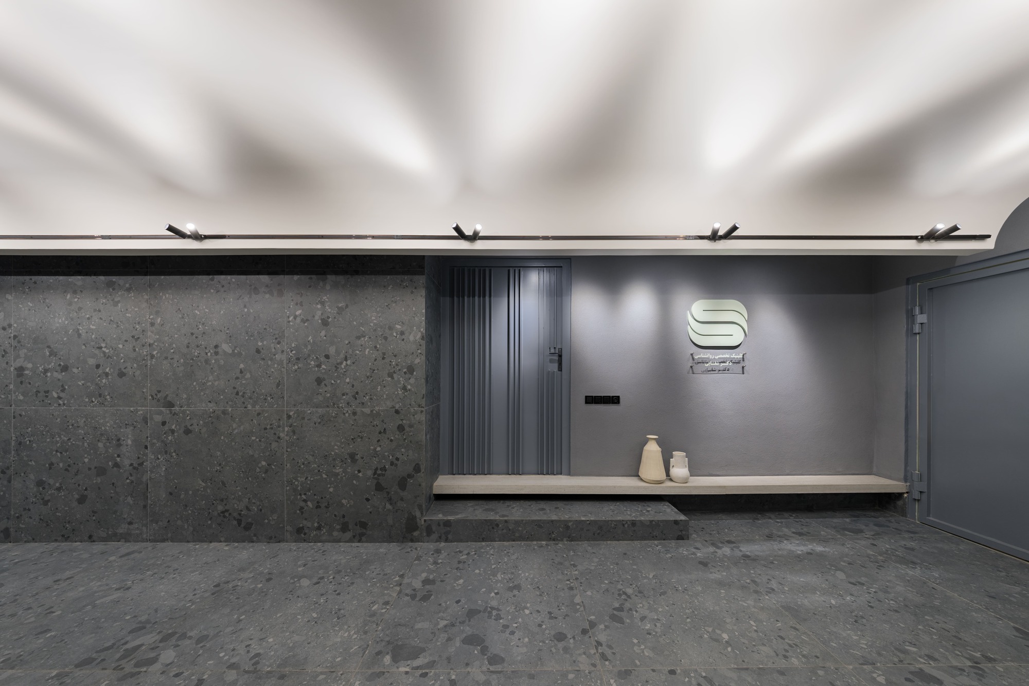Reception desk with illuminated signage and concrete wall beneath an exposed ceiling with track lighting