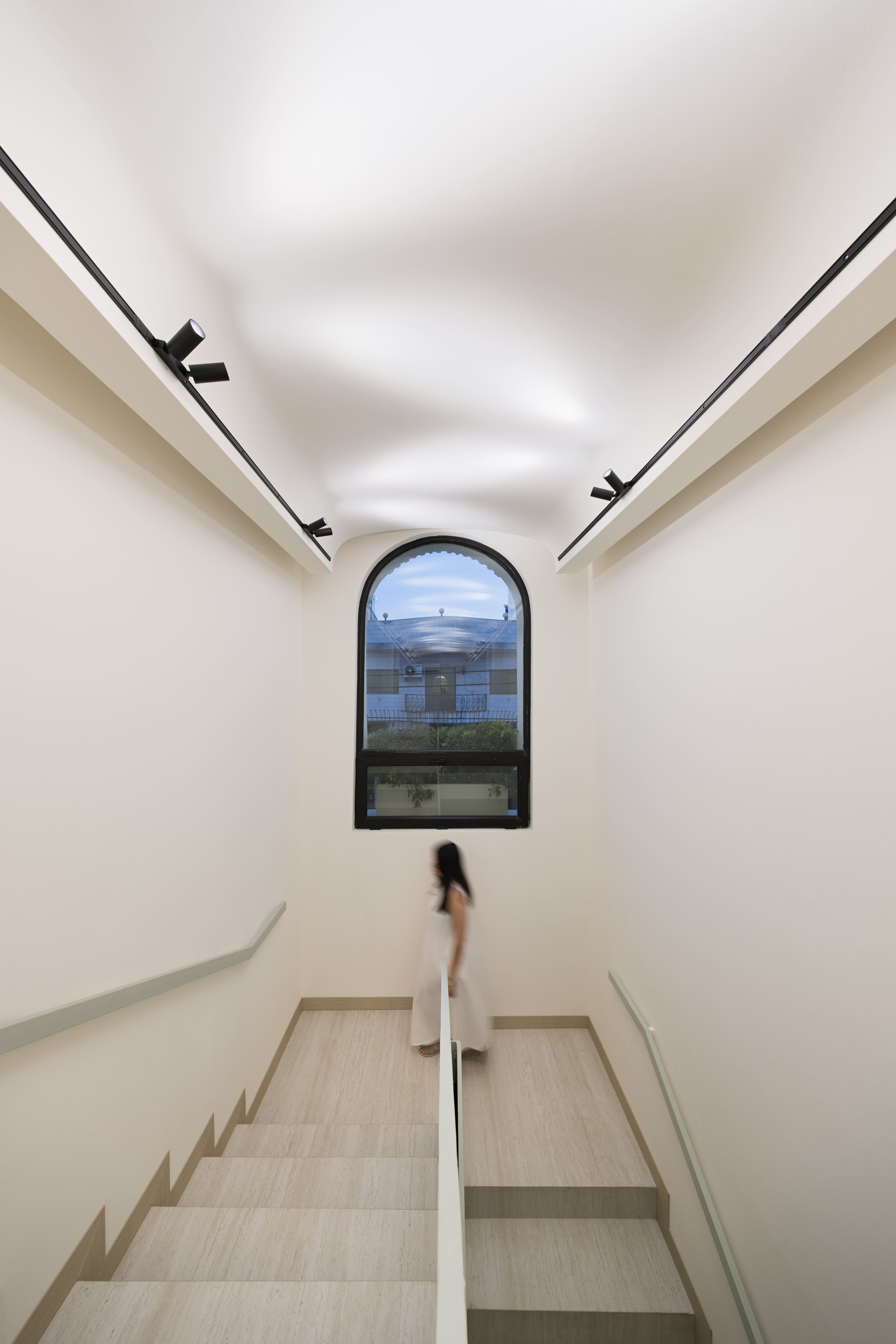 Interior stairwell with arched window at the landing and a figure descending the pale stone steps
