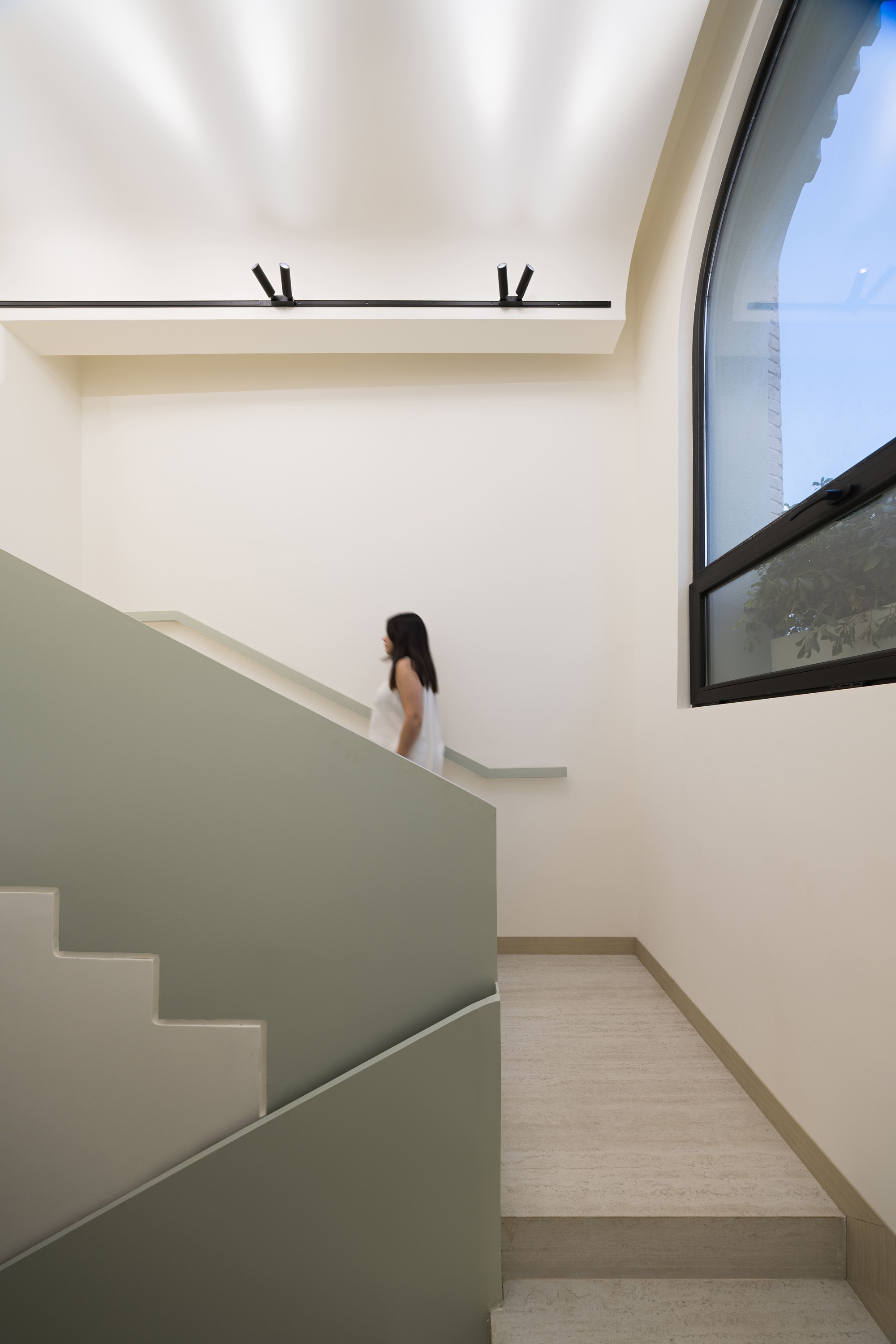 Staircase with sage green wall panels and linear skylight above a person on the upper landing