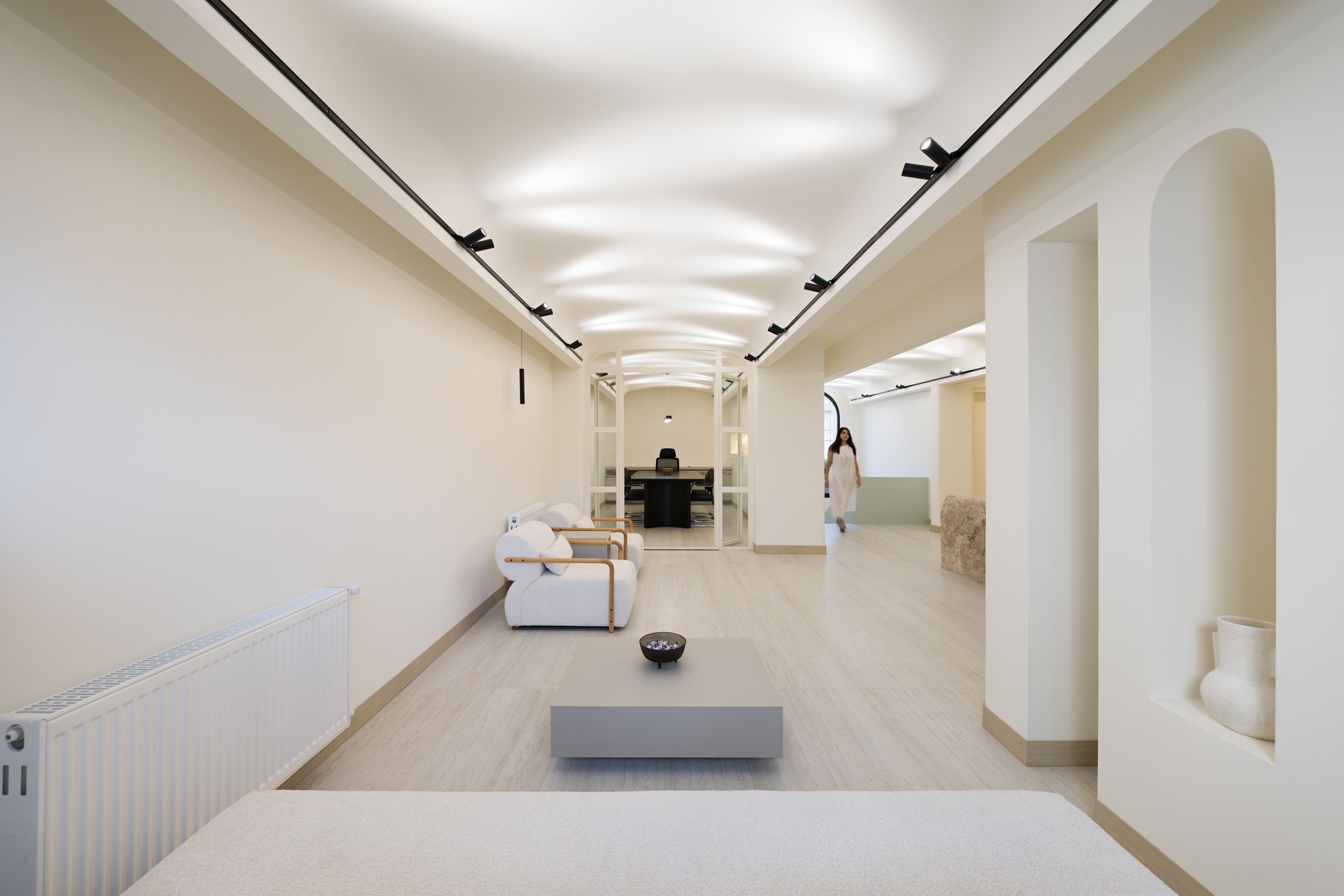 Corridor with vaulted ceiling and recessed track lighting connecting reception areas with seating and archways