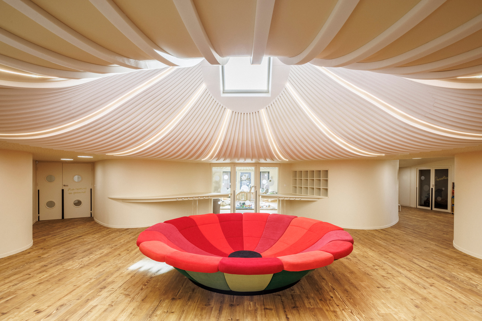 Interior with pleated fabric ceiling radiating from a central skylight above a red petal-shaped seating element