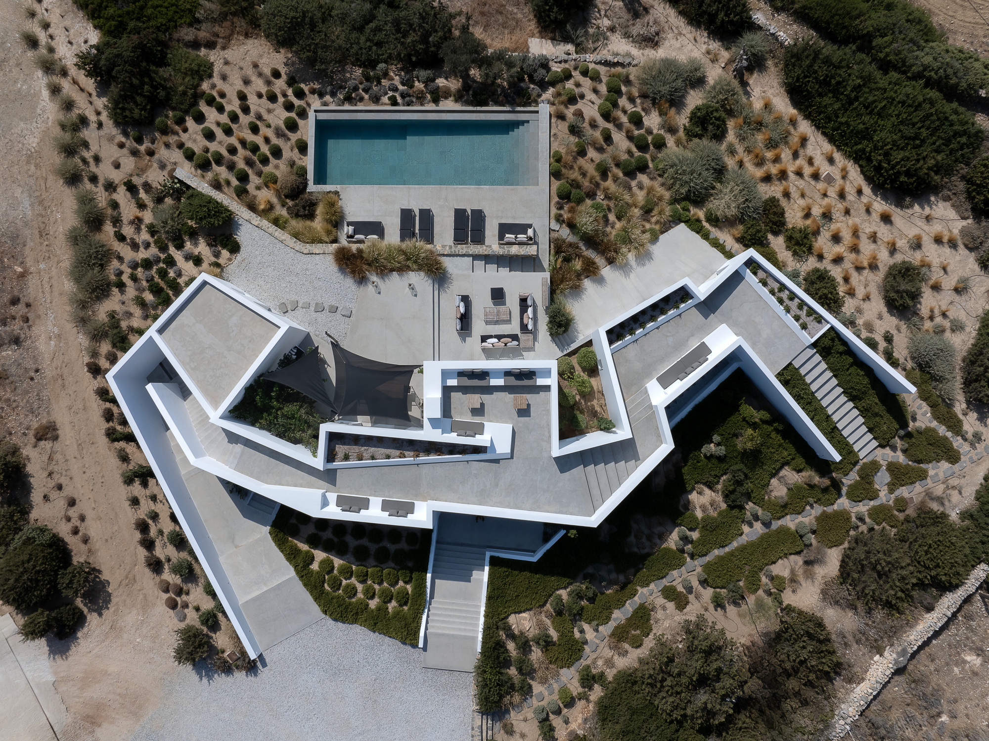 Drone view showing the angular white roofscape with central courtyard pool and surrounding olive groves