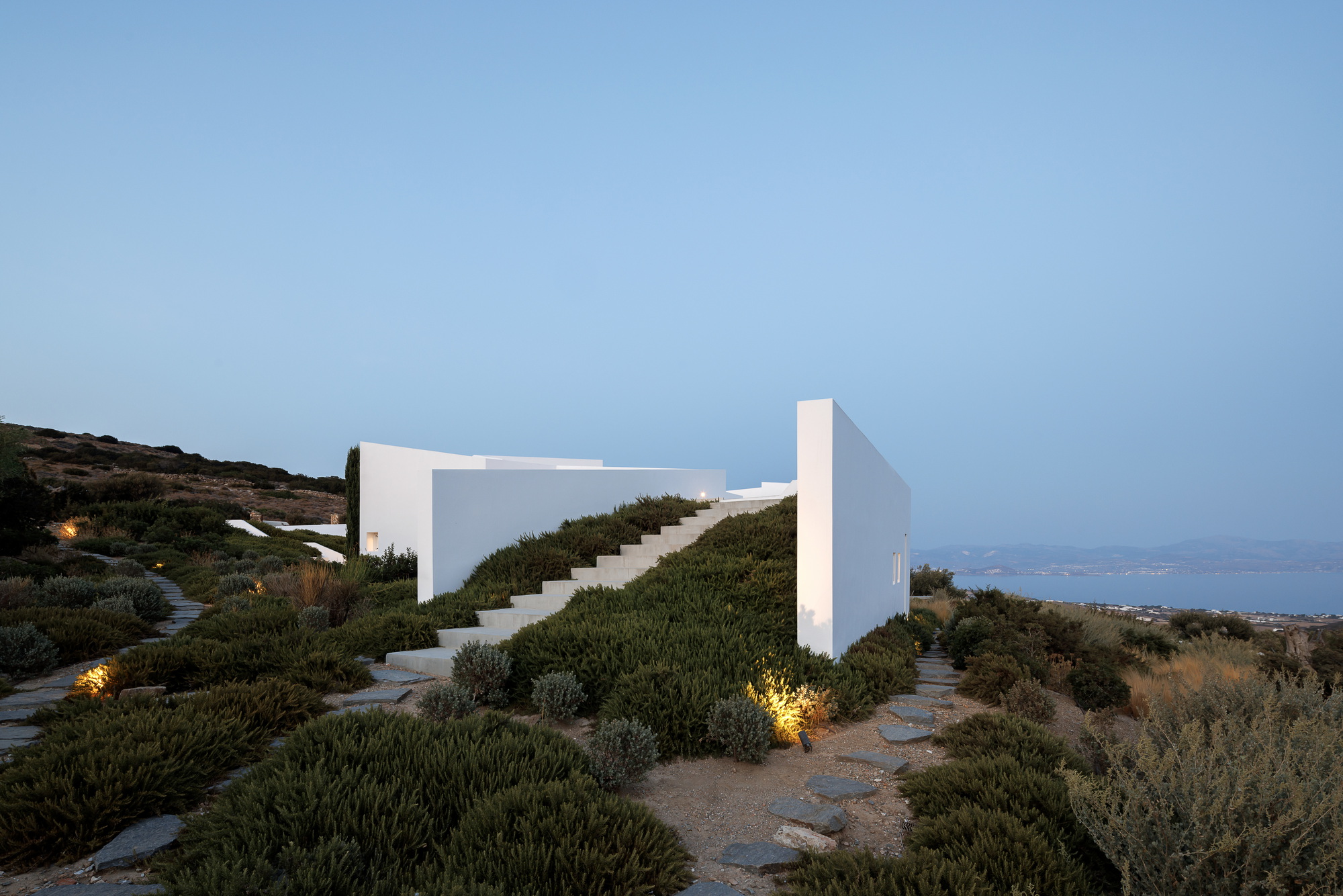 Exterior staircase framed by white rendered walls emerging from groundcover planting at dusk