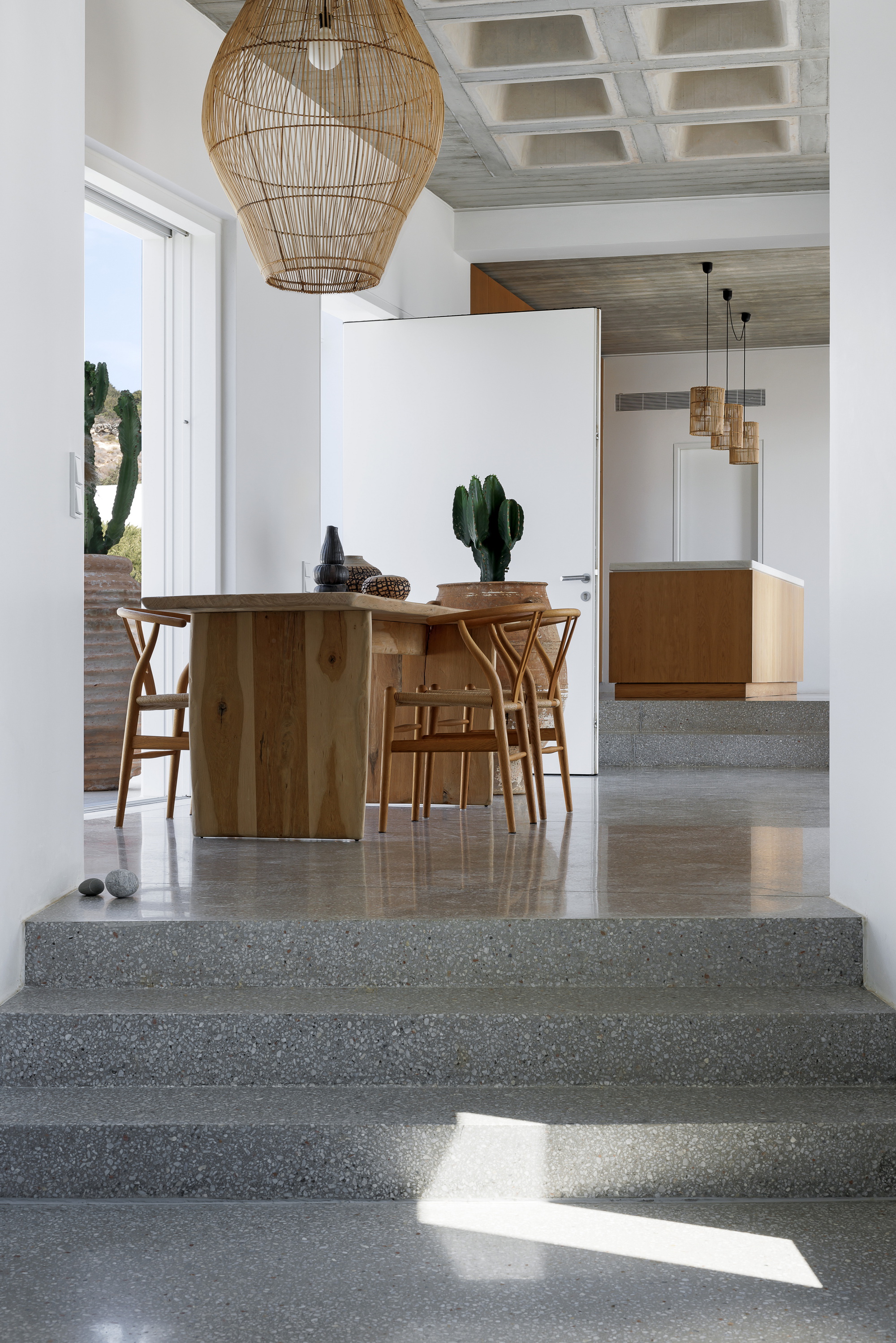 Polished terrazzo steps leading to the dining area with wooden table and woven pendant lights