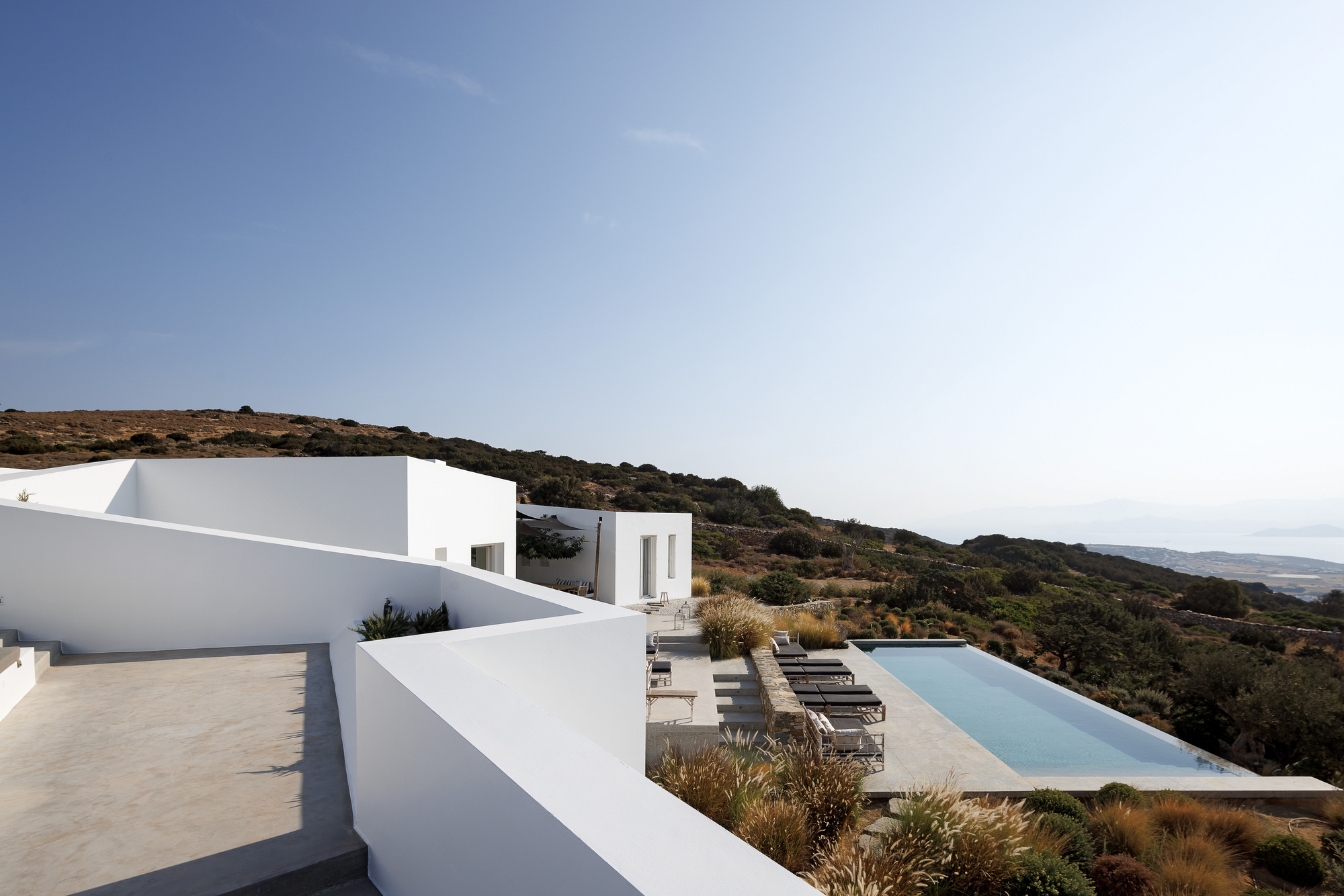 Infinity pool deck with loungers and grasses overlooking the sloping landscape