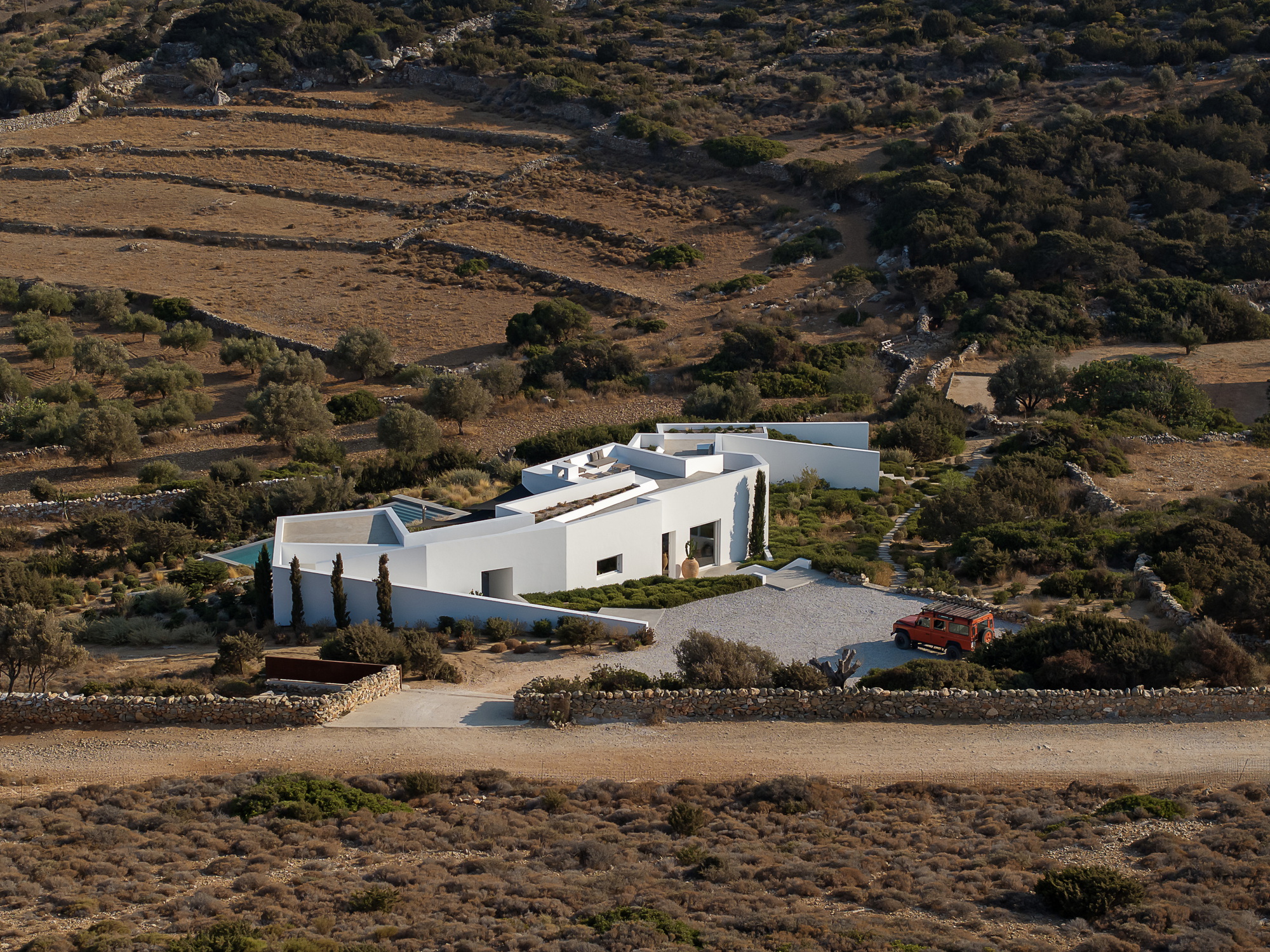 White compound nestled in a hillside landscape with terraced fields and sparse vegetation