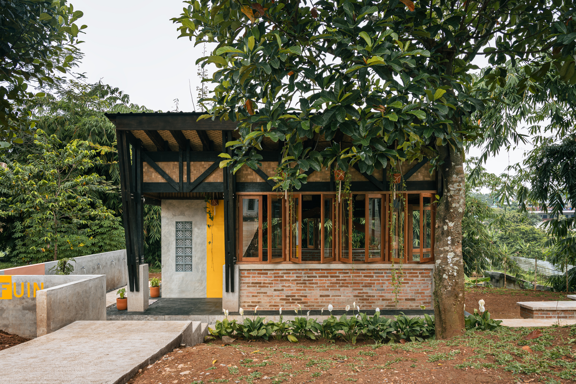 Single-story pavilion with exposed timber rafters, brick walls and timber-framed glazing beneath fruit trees